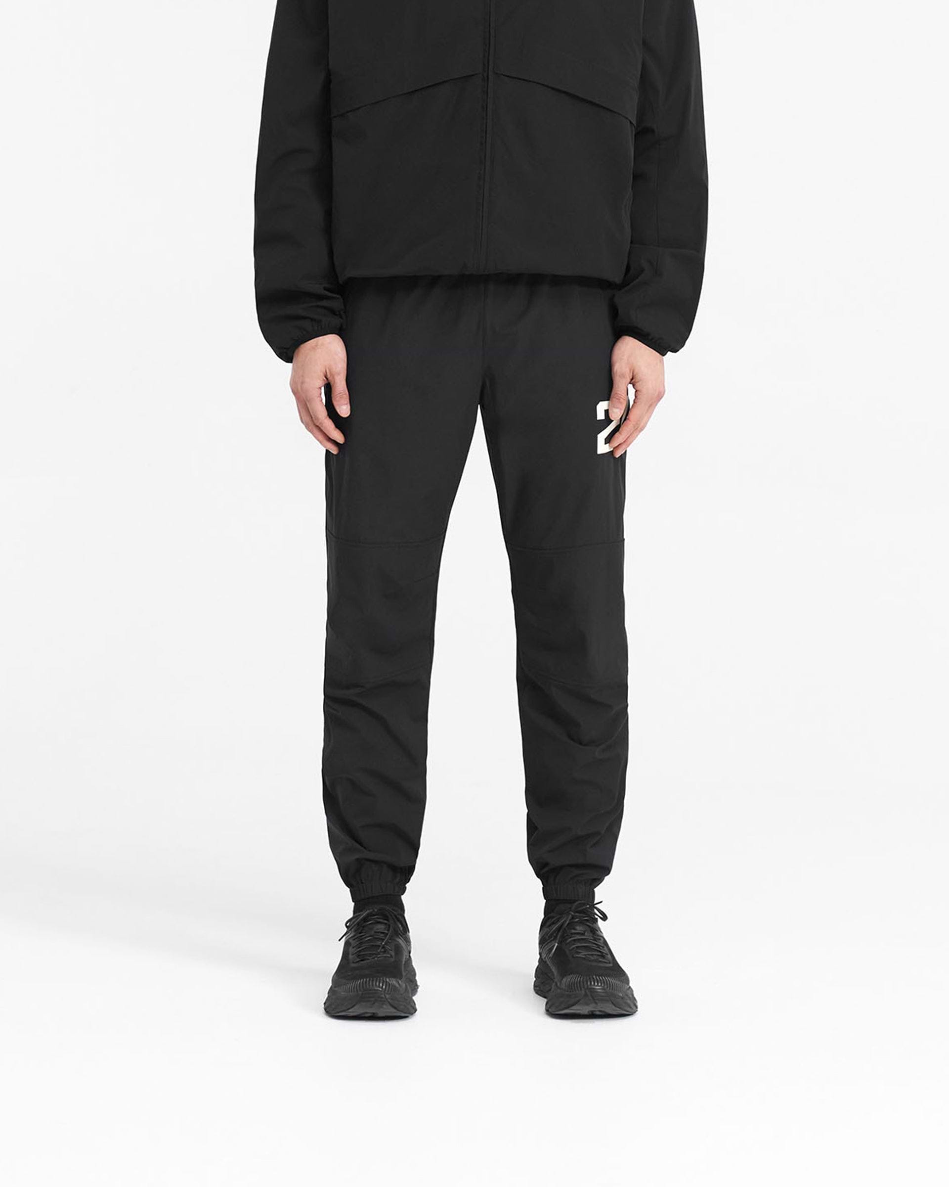 Man wearing black pants on a plain white background | 247 Training Pant in Jet Black | Training pants with zip pockets and elasticated waistband | 247 Pants | Represent Clo