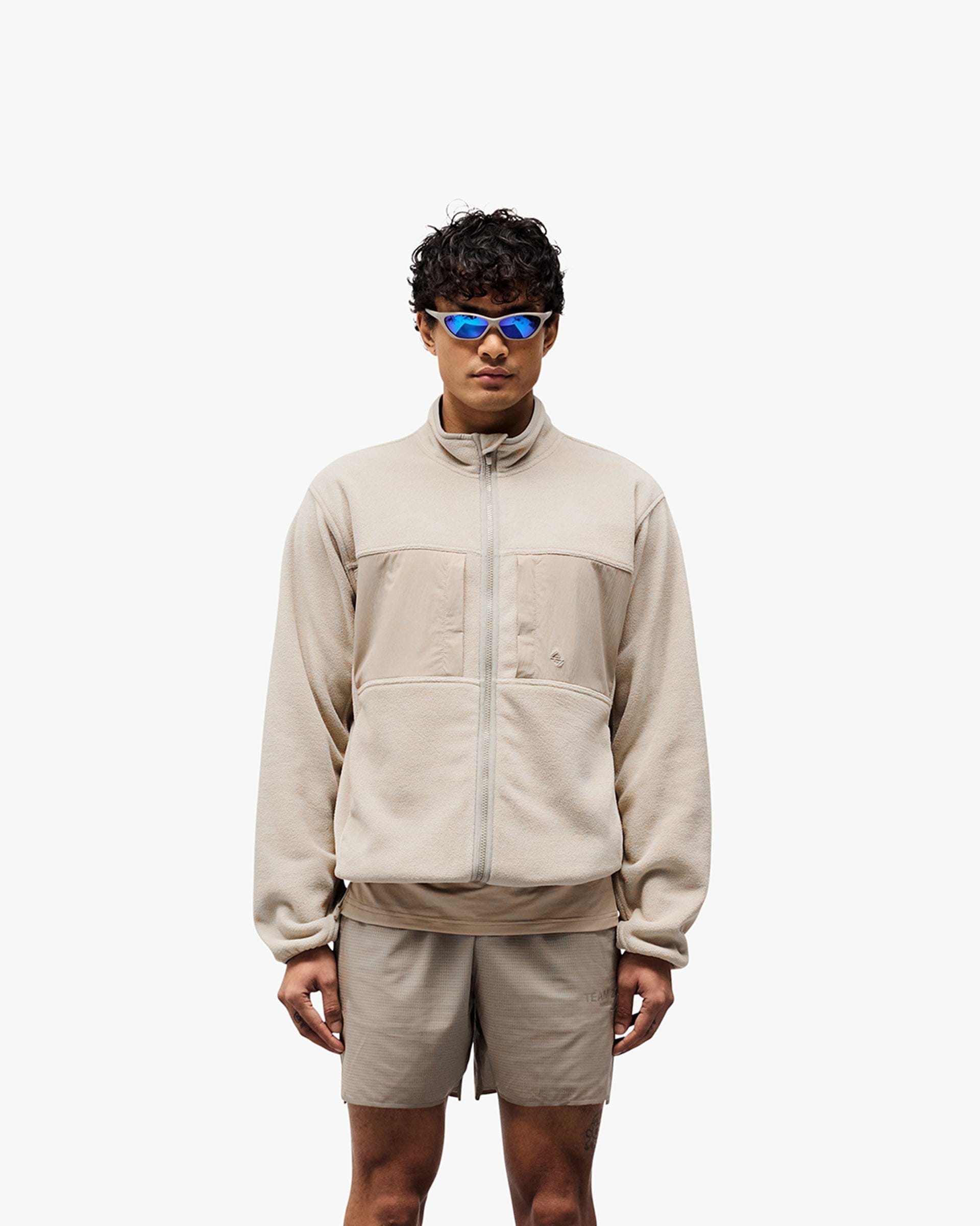 Man wearing a grey fleece on a plain white background | 247 Polar Panelled Fleece in Pebble | Fleece with toggle hem and zip pockets | 247 Outerwear | Represent Clo