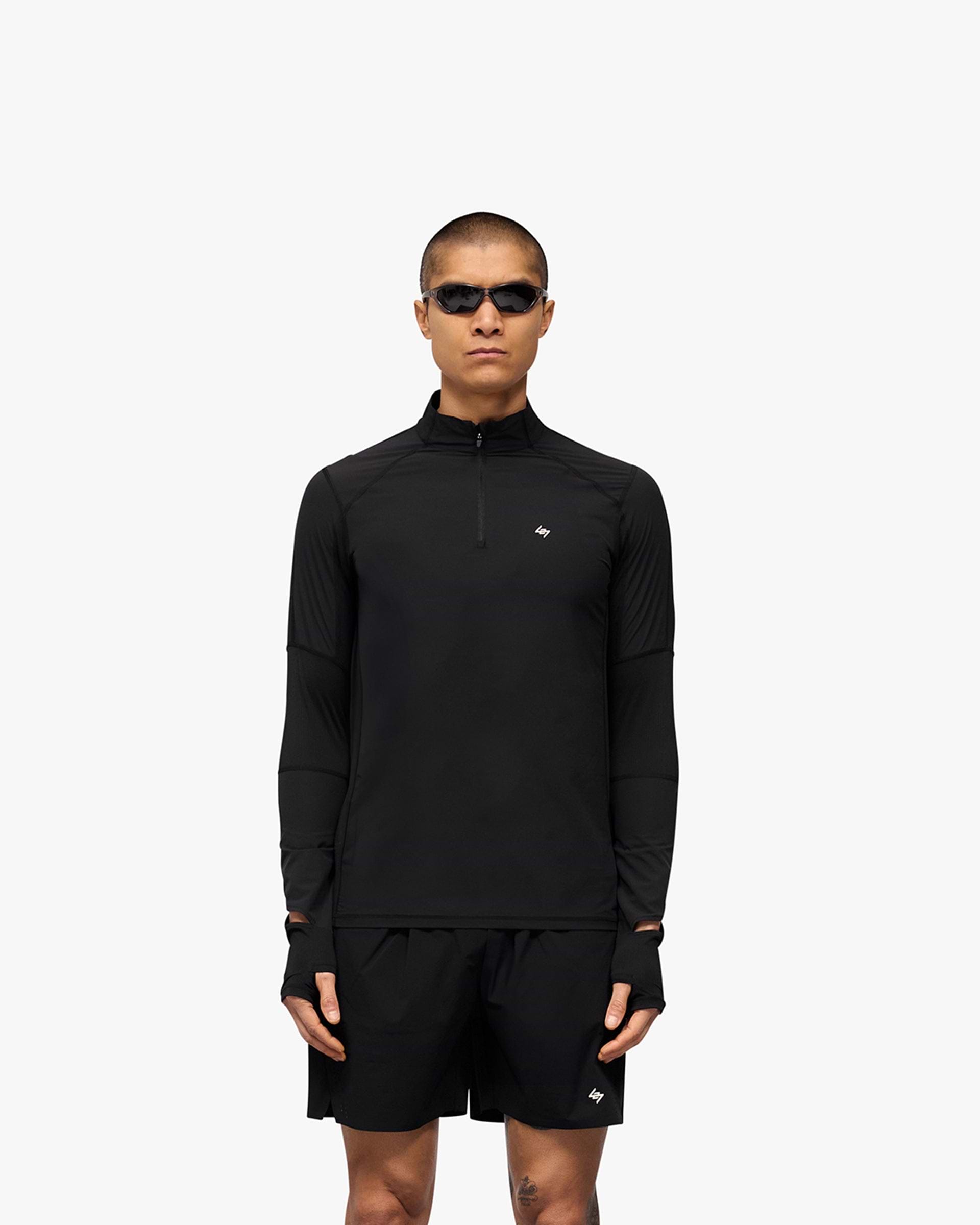Man wearing a black quarter zip top on a plain white background | 247 Run Quarter Zip in Jet Black | Performance outerwear with mesh panels and thumb holes | 247 Outerwear | Represent Clo
