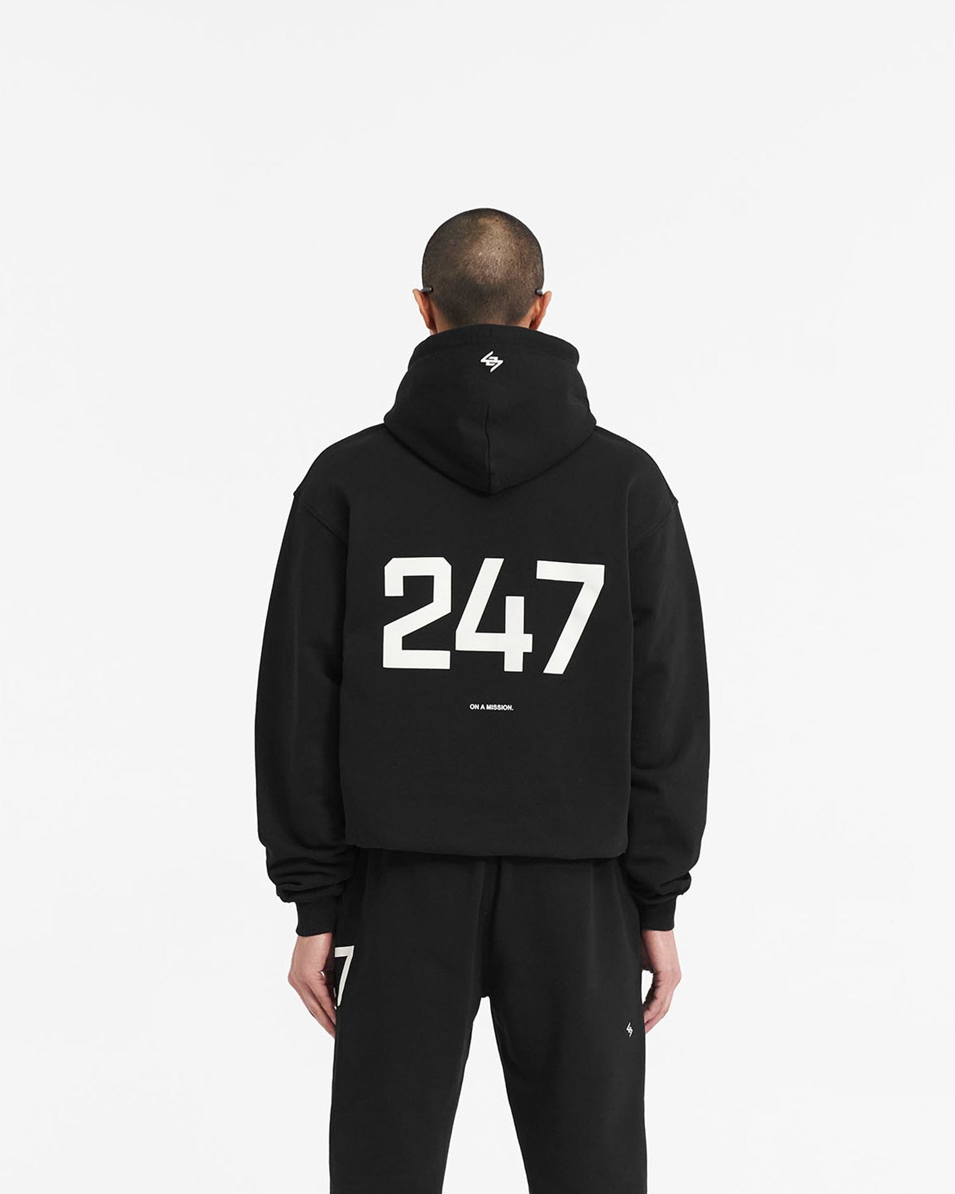 Man wearing a black hooded jacket on a plain white background | 247 Hooded Training Jacket in Jet Black | Nylon jacket with DWR coating and adjustable hem | 247 Outerwear | Represent Clo