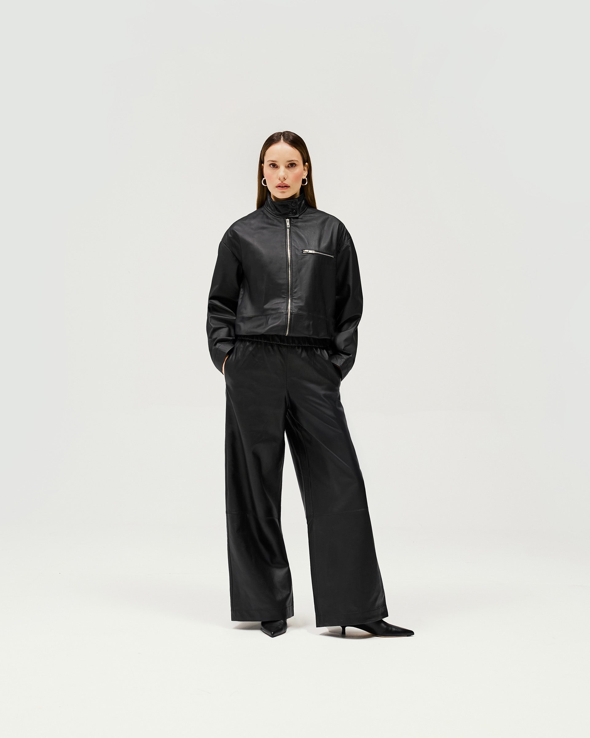 Woman wearing a black leather jacket on a plain white background | Fuel Jacket in Jet Black | Sportswear inspired jacket with elasticated gathered waist | Womens SS25 Outerwear | Represent Clo