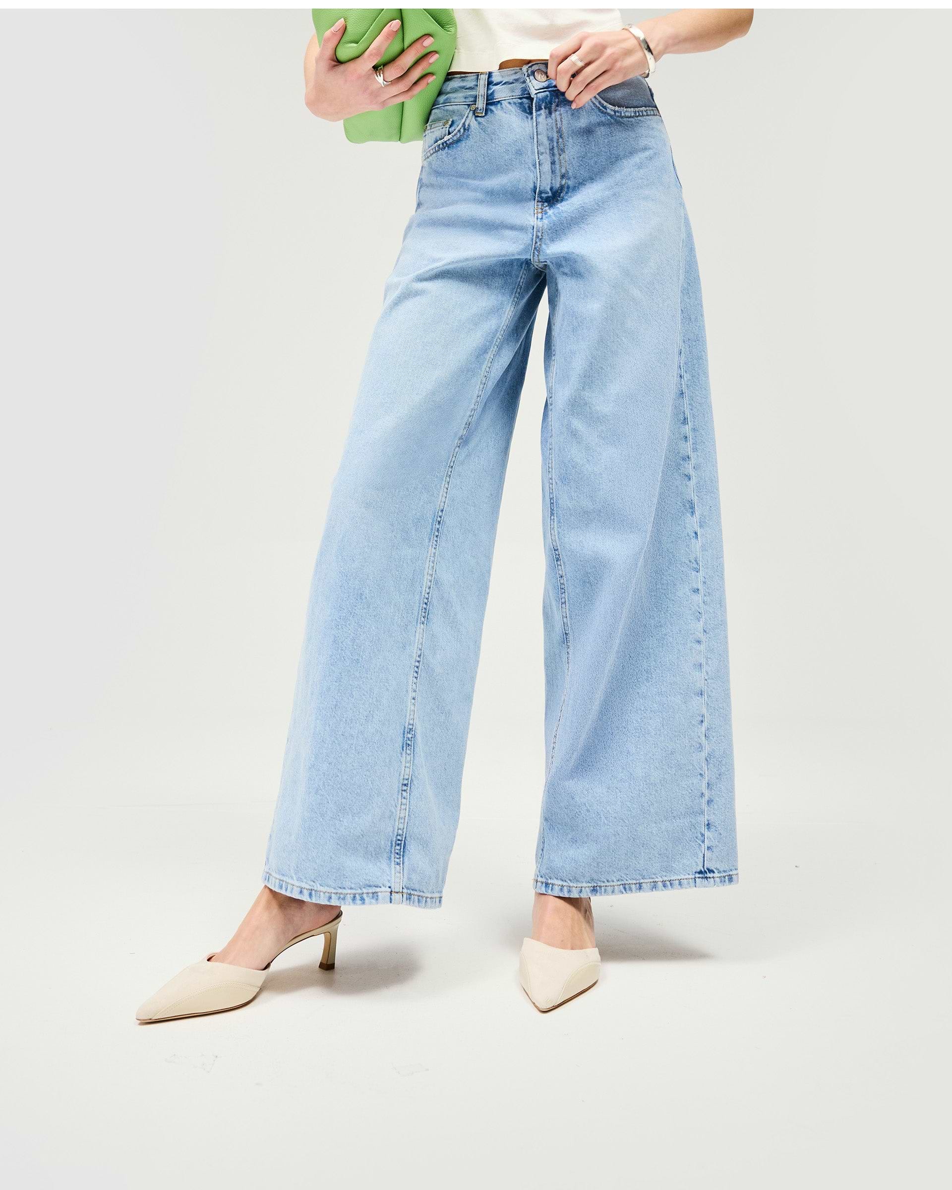 Woman wearing mid-rise wide-leg jeans in blue on a plain white background | Mid Rise Wide Leg Jean in Washed Blue | Relaxed wide leg jeans with nickel rivets | Womens SS25 Jeans | Represent Clo
