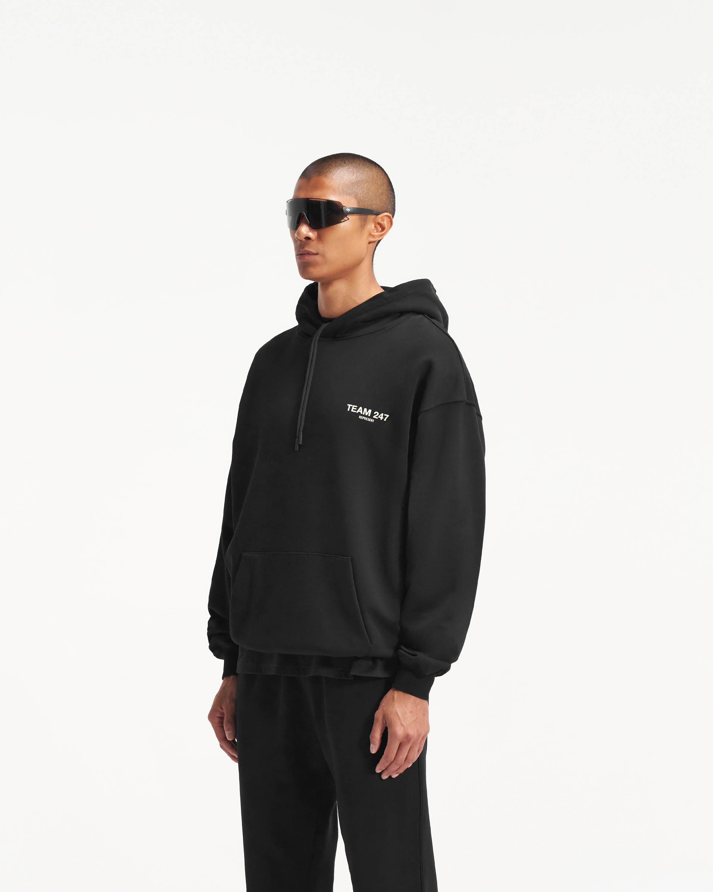 Man wearing a black oversized hoodie on a plain white background | Team 247 Oversized Hoodie in Black | Hoodie with ribbed cuffs and hem | 247 Hoodies | Represent Clo