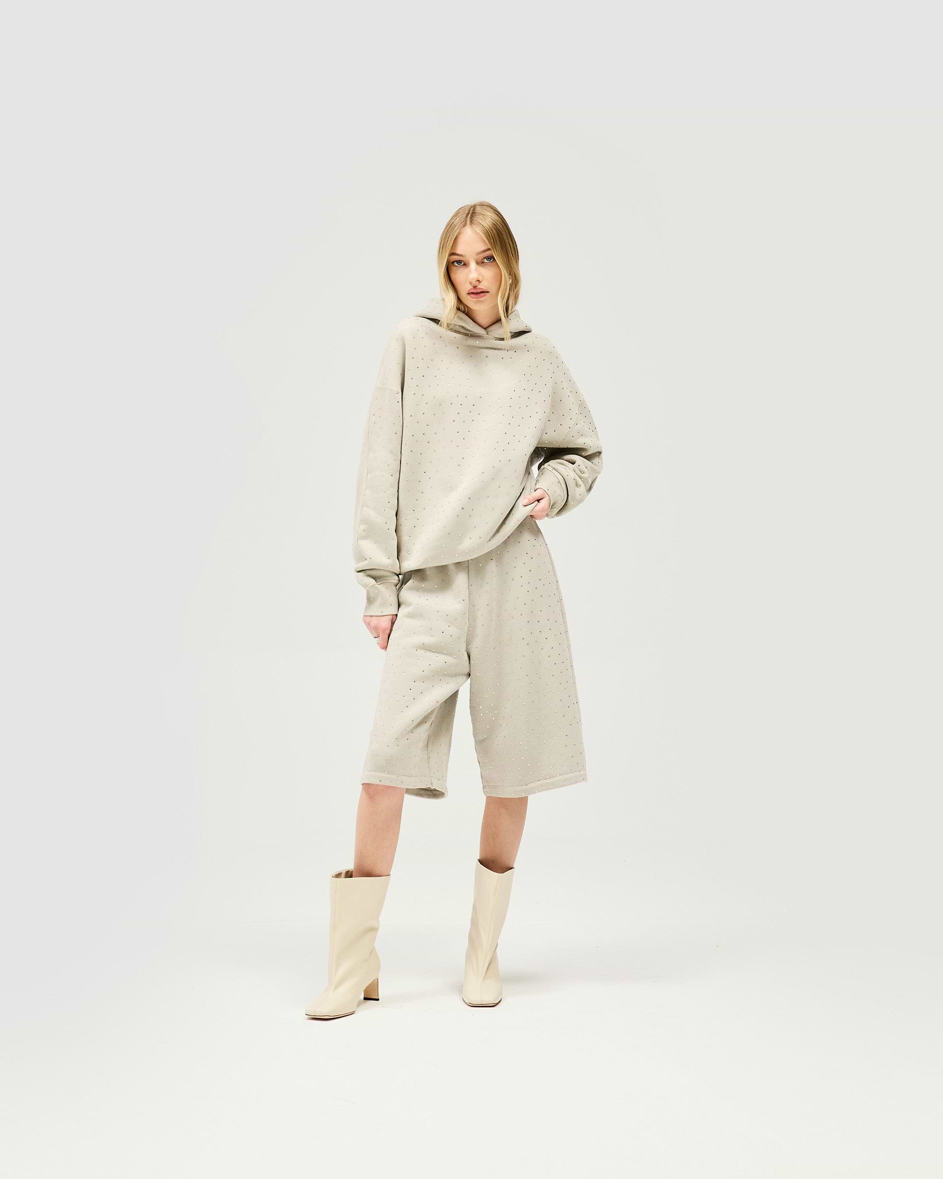 Woman wearing an oversized grey hoodie on a plain white background | Spark Hoodie in Storm | Slouchy hoodie with all over hotfix detailing | Womens SS25 Hoodies | Represent Clo