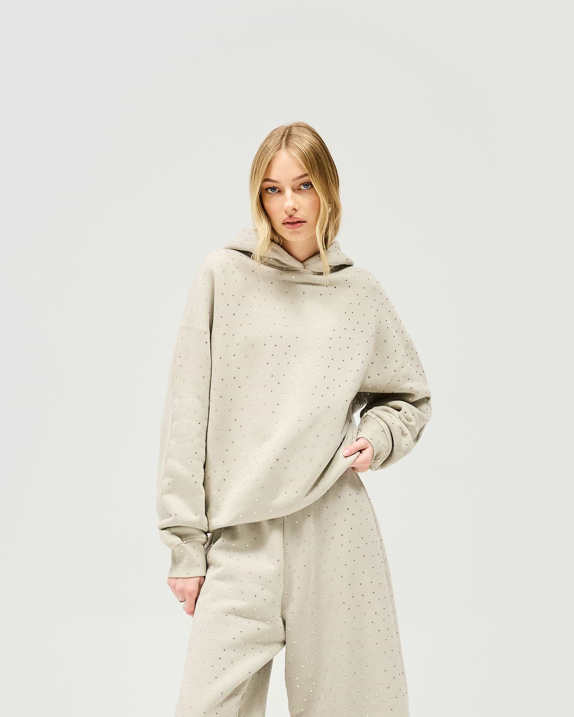 Woman wearing an oversized grey hoodie with acid wash on a plain white background | Spark Hoodie in Storm | Oversized hoodie with all over hotfix | Womens SS25 Hoodies | Represent Clo
