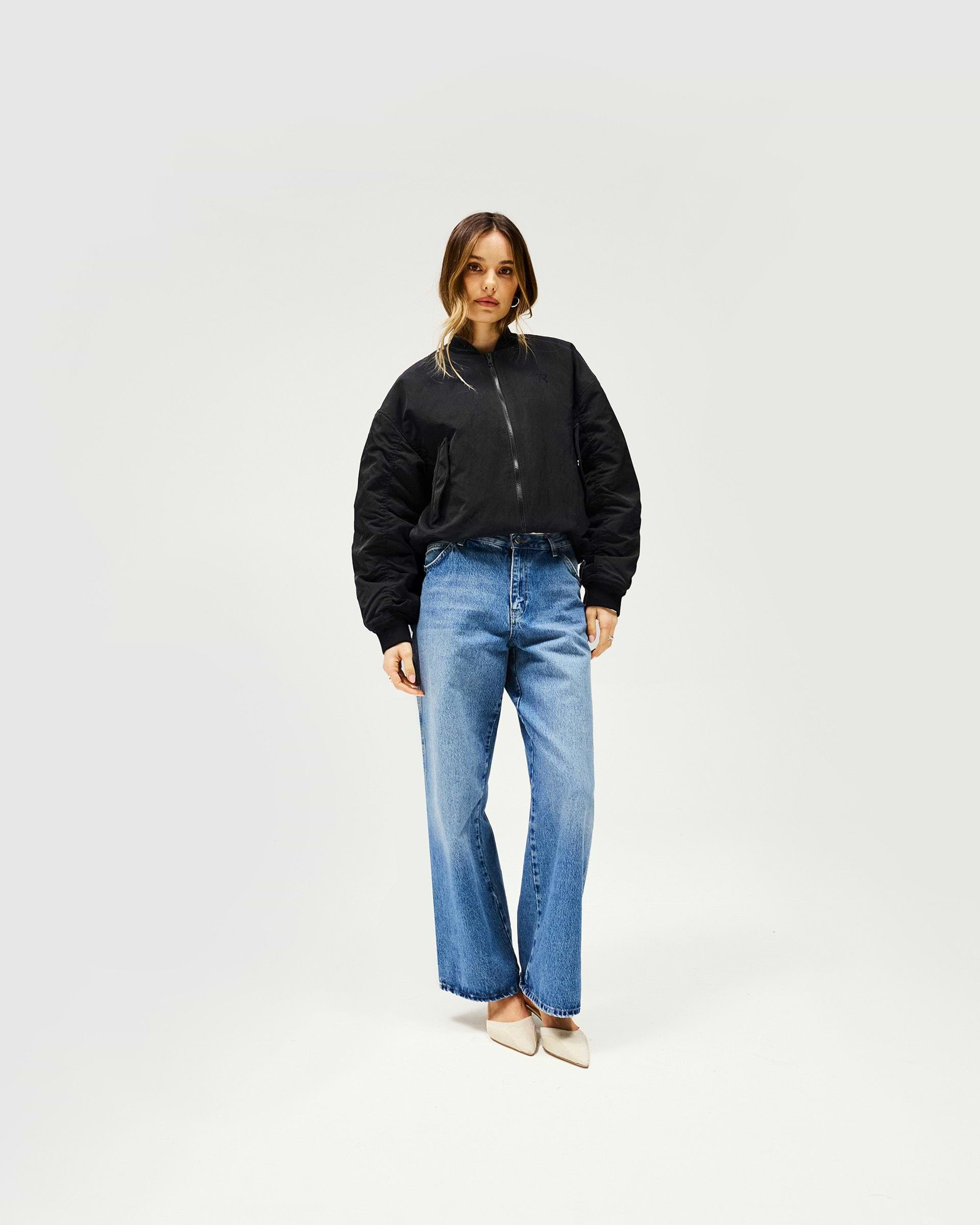 Woman wearing a black oversized bomber jacket on a plain white background | Subway Jacket in Jet Black | Nylon bomber with embroidered logo and ribbed cuffs | Womens SS25 Outerwear | Represent Clo