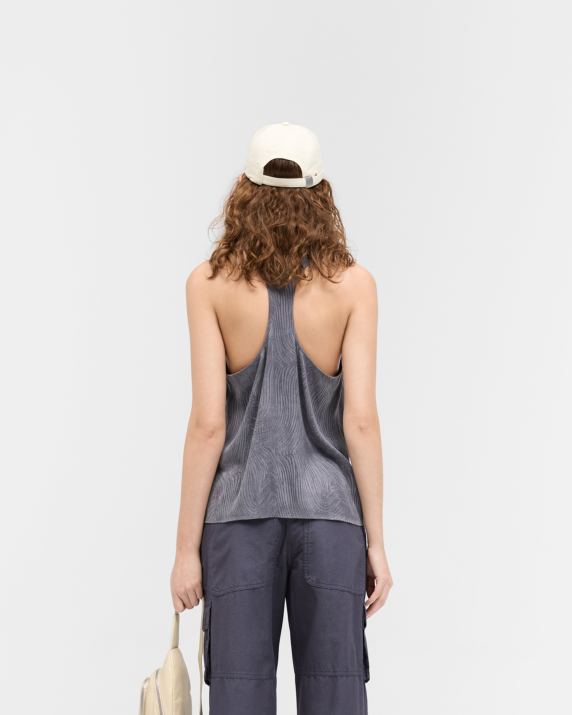 Woman wearing a black swirl top on a plain white background | Swirl Top in Jet Black | Low cut vest top with dropped neckline and racer back | Womens SS25 Tops | Represent Clo
