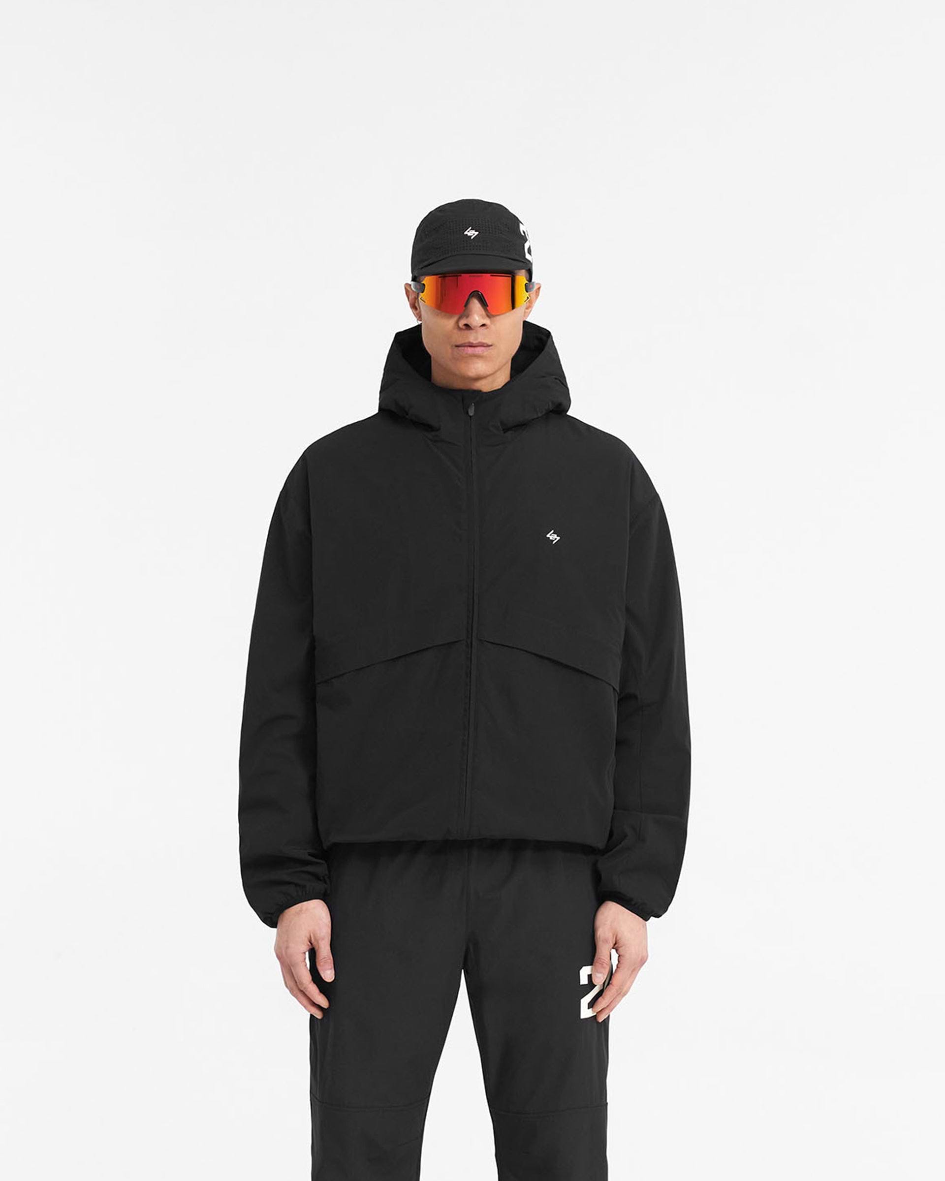 Man wearing a black hooded training jacket on a plain white background | 247 Hooded Training Jacket in Jet Black | Nylon jacket with DWR coating and adjustable hem | 247 Outerwear | Represent Clo