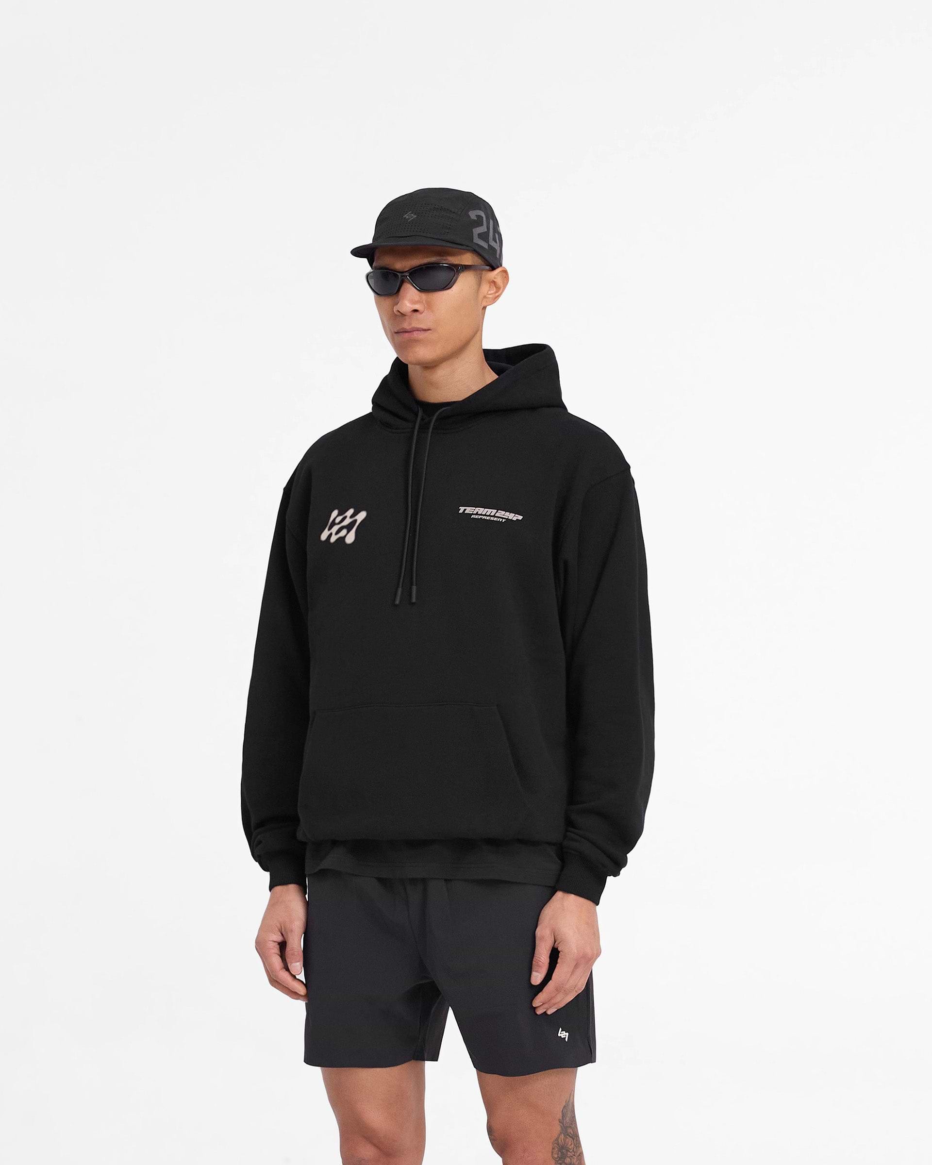 Man wearing an oversized black hoodie on a plain white background | 247 Future Terrains Oversized Hoodie in Black | Heavyweight cotton hoodie with Team 247 branding | 247 Hoodies | Represent Clo