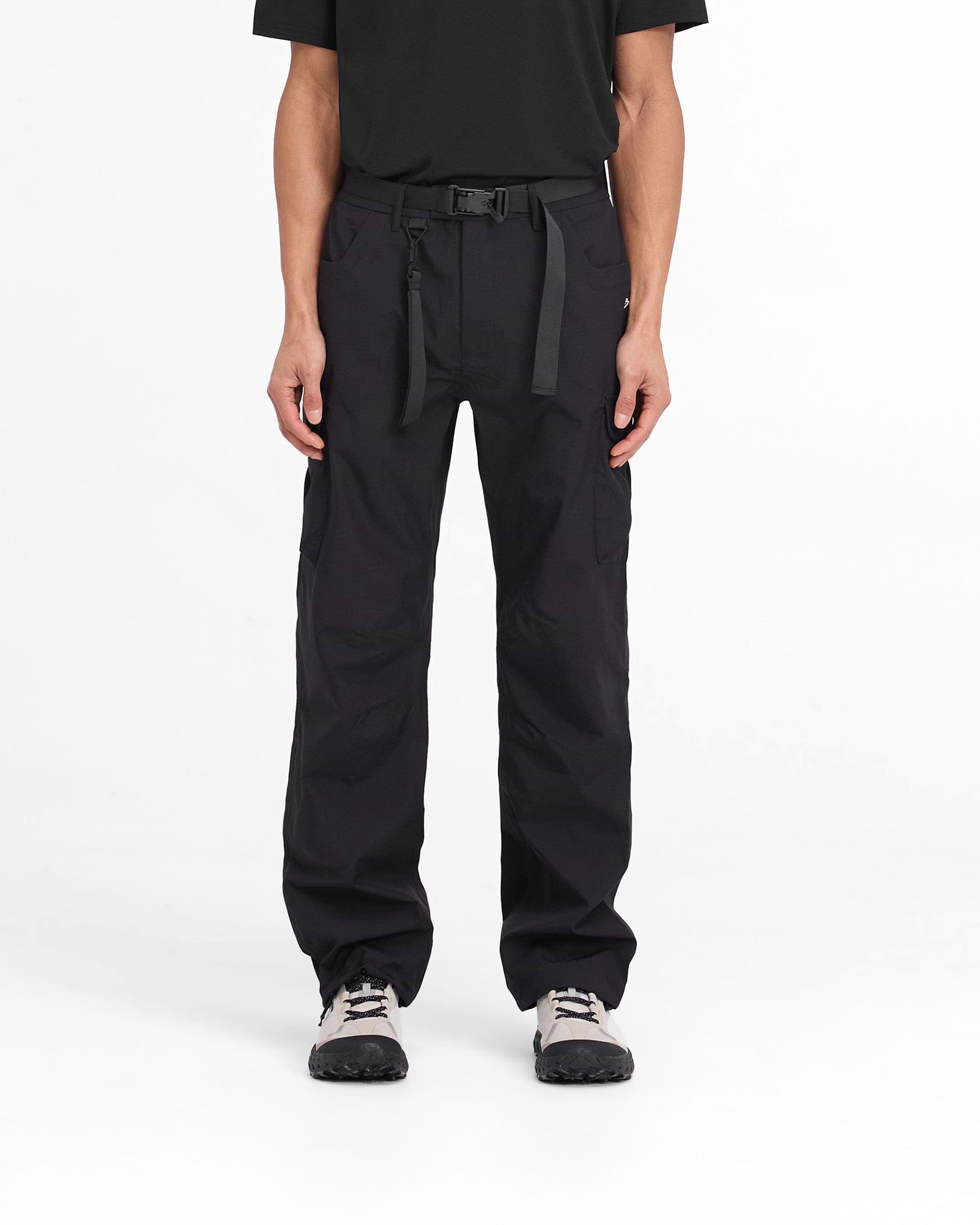 Man wearing black technical cargo pants on a plain white background | 247 Technical Cargo Pant in Black | Showerproof cargos with maglock buckle | 247 Pants | Represent Clo