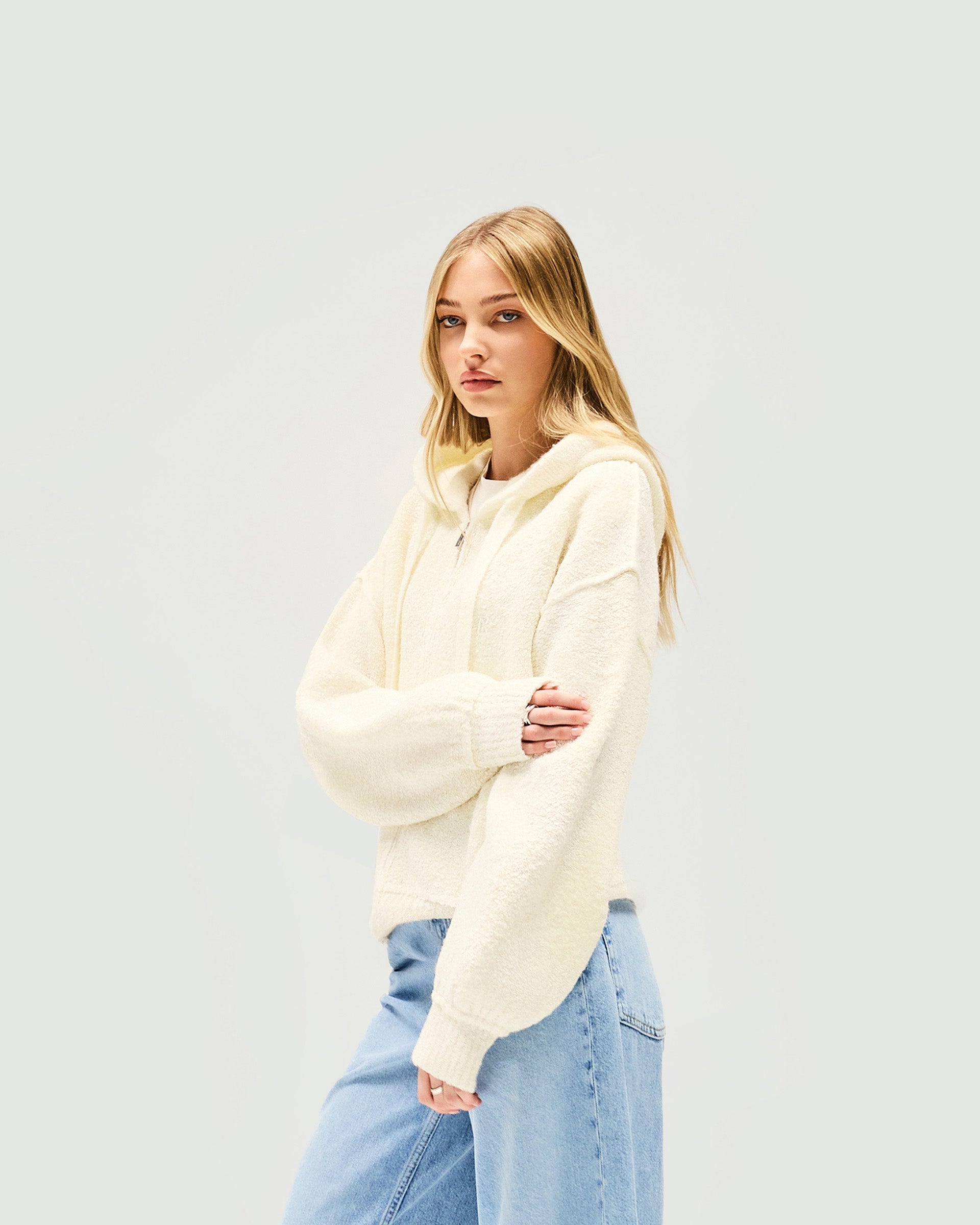 Woman wearing a knitted white hoodie on a plain white background | Whip Hoodie in Antique White | Knitted hoodie with zipper and seaming detail | Womens SS25 Knitwear | Represent Clo