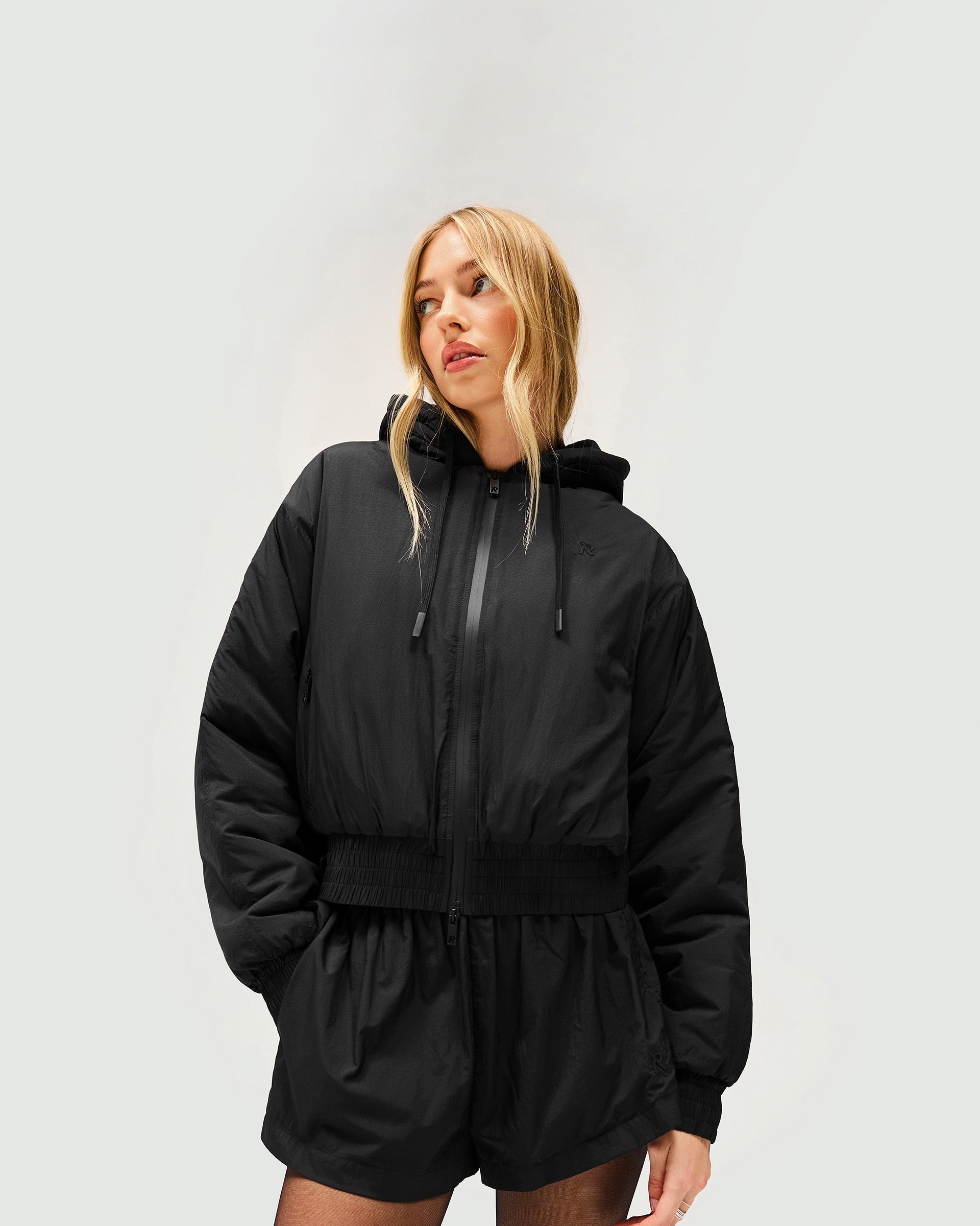 Woman wearing an underground nylon jacket in black on a plain white background | Underground Jacket in Jet Black | Relaxed fit flyaway jacket with silicon dipped drawcords | Womens SS25 Outerwear | Represent Clo