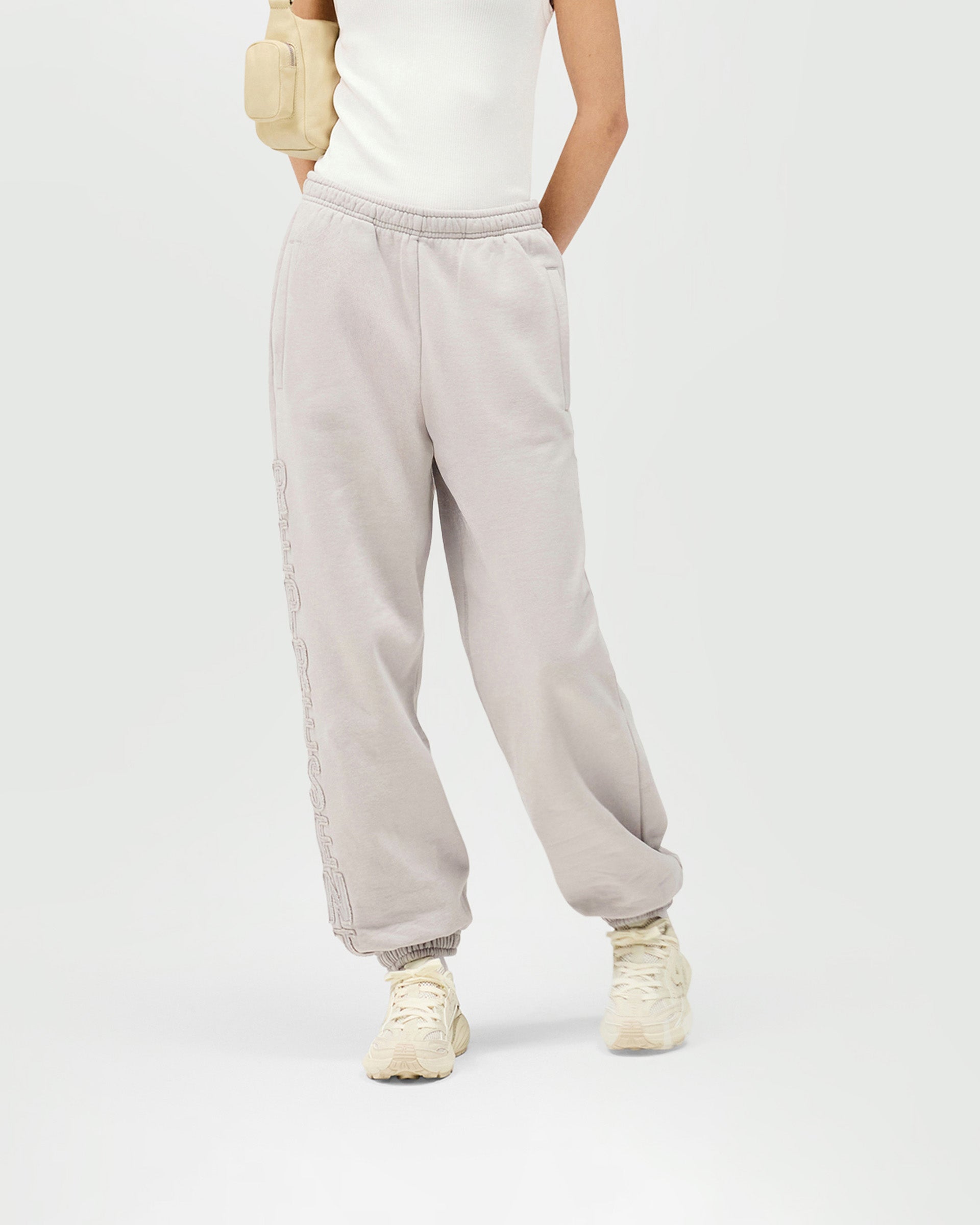 Woman wearing light grey joggers on a plain white background | Epic Jogger in Light Grey | Relaxed fit joggers with raw edge branding | Womens SS25 Bottoms | Represent Clo