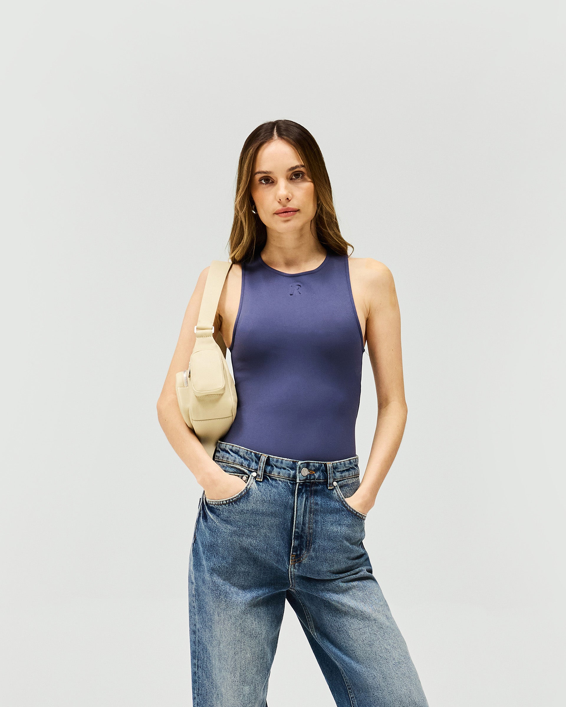 Woman wearing a grey minimalist bodysuit on a plain white background | Control Bodysuit in Graphite | Bodysuit with rounded neckline and thong back | Womens SS25 Tops | Represent Clo