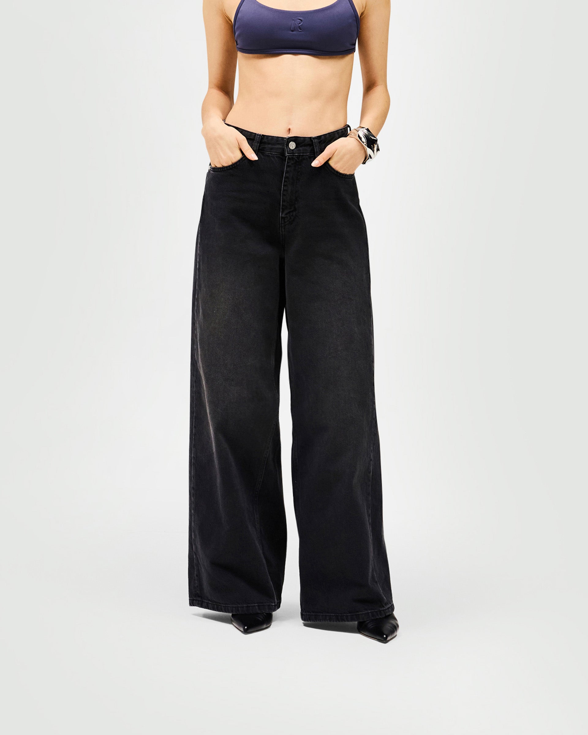 Woman wearing black wide-leg jeans on a plain white background | Mid Rise Wide Leg Jean in Washed Black | Wide leg jeans with leather branded patch | Womens SS25 Jeans | Represent Clo