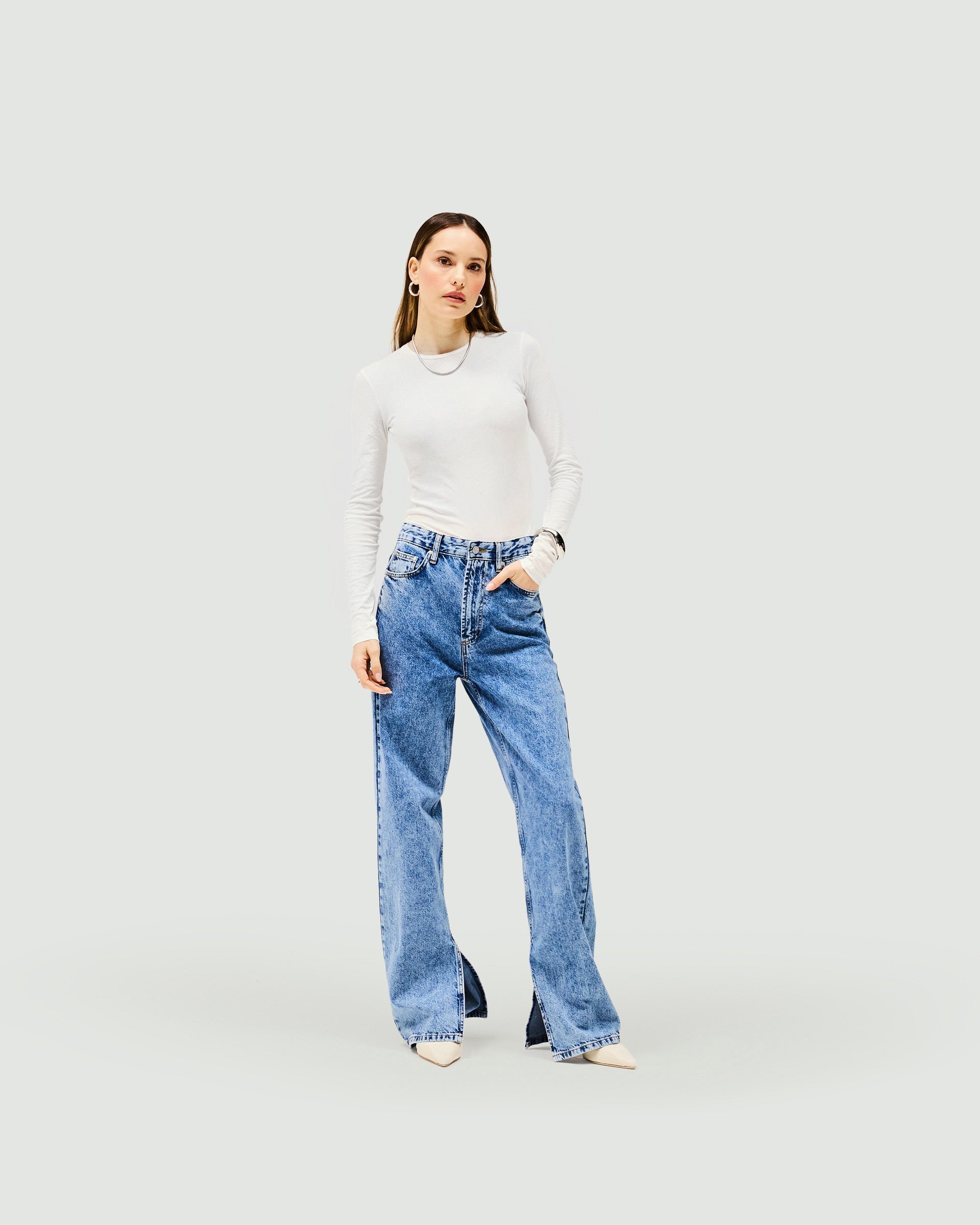 Woman wearing washed blue jeans with split hem on a plain white background | Split Hem Straight Jean in Washed Blue | Straight leg jeans with outside seam split | Womens SS25 Jeans | Represent Clo