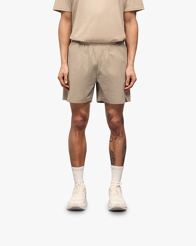 Man wearing grey shorts on a plain white background | 247 Training Shorts in Pebble | Nylon blend shorts with zip pockets and perforation detailing | 247 Shorts | Represent Clo