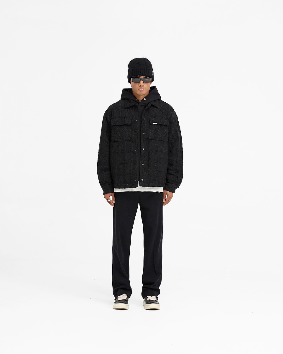 Man wearing a black overshirt on a plain white background | Wadded Overshirt in Black | Oversized black overshirt with matte popper closures | FW24 Shirts | Represent Clo