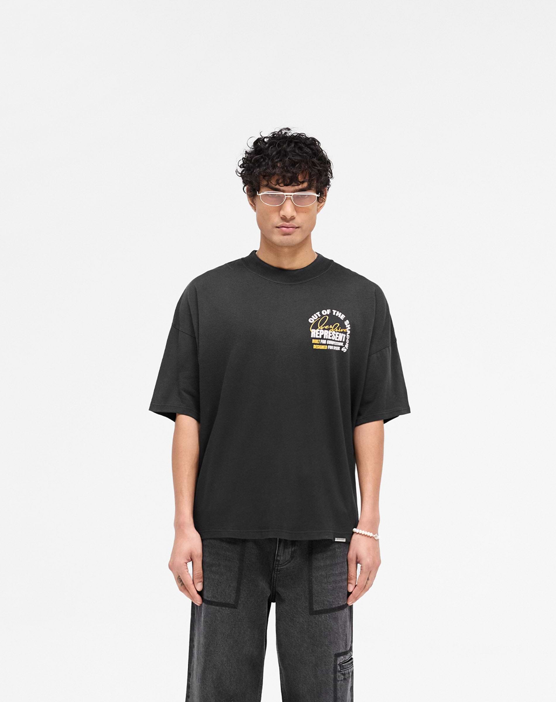 Man wearing a black graphic t-shirt on a plain white background | Out Of The Shadows T-Shirt in Stained Black | Boxy fit with fade out wash and metal bar hem | SS25 T-Shirts | Represent Clo