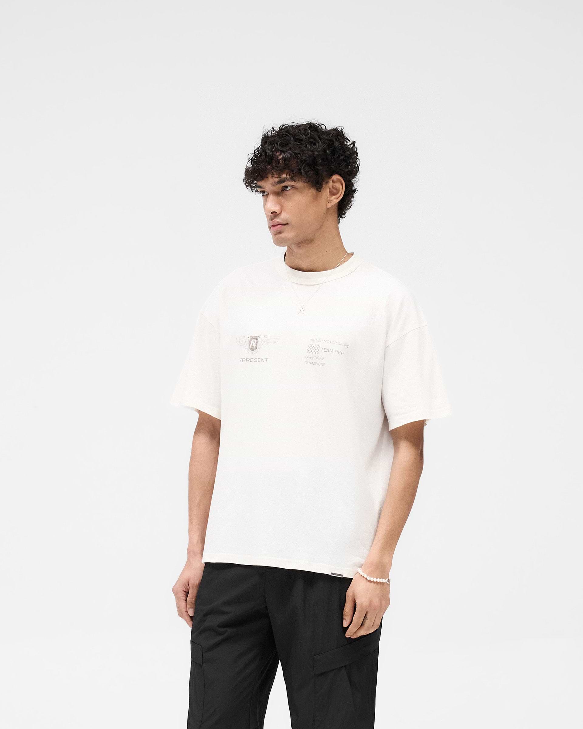 Man wearing a white t-shirt on a plain white background | Team Rep T-Shirt in Flat White | Oversized t-shirt with Represent logo metal bar | SS25 T-Shirts | Represent Clo