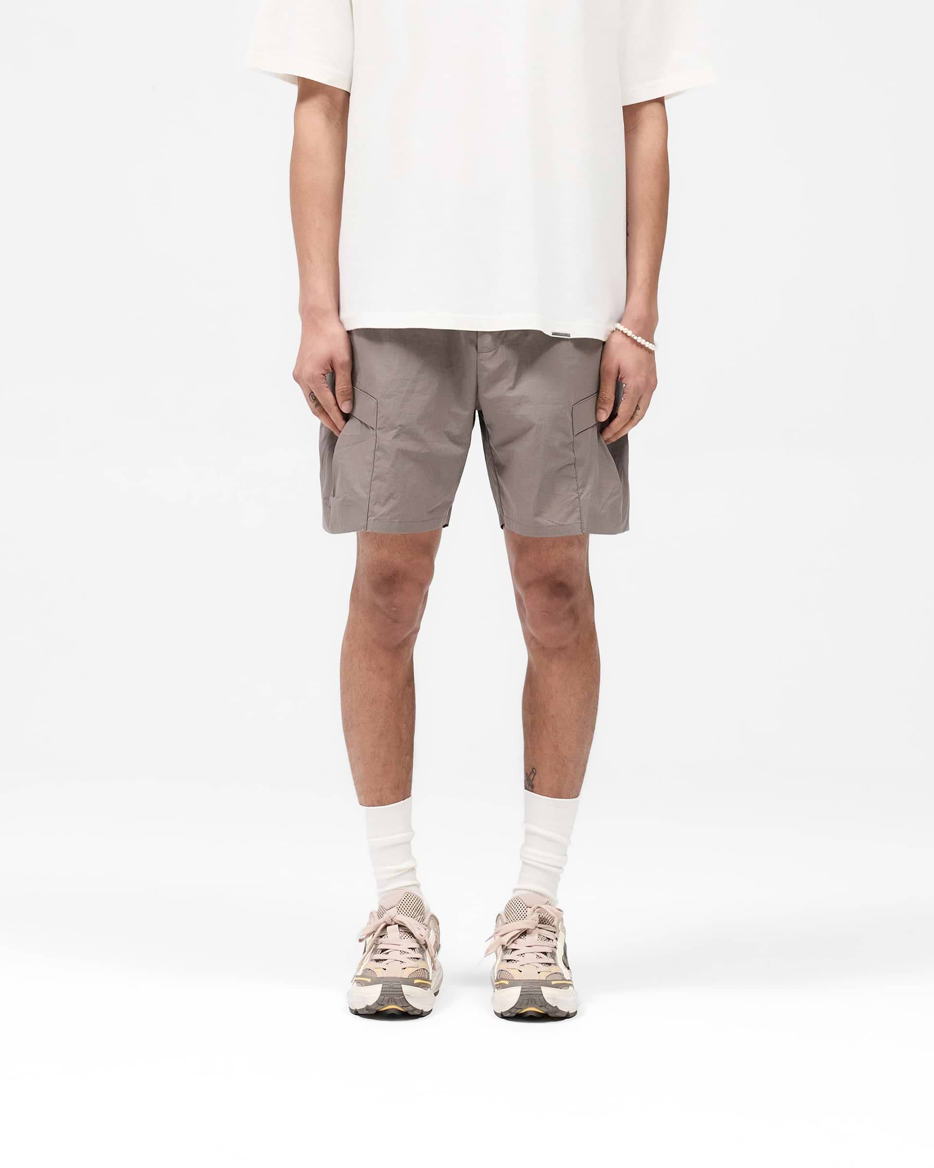 Man wearing mid-grey cargo shorts on a plain white background | Tech Cargo Short in Mid Grey | Lightweight shorts with pleated cargo pockets | SS25 Shorts | Represent Clo