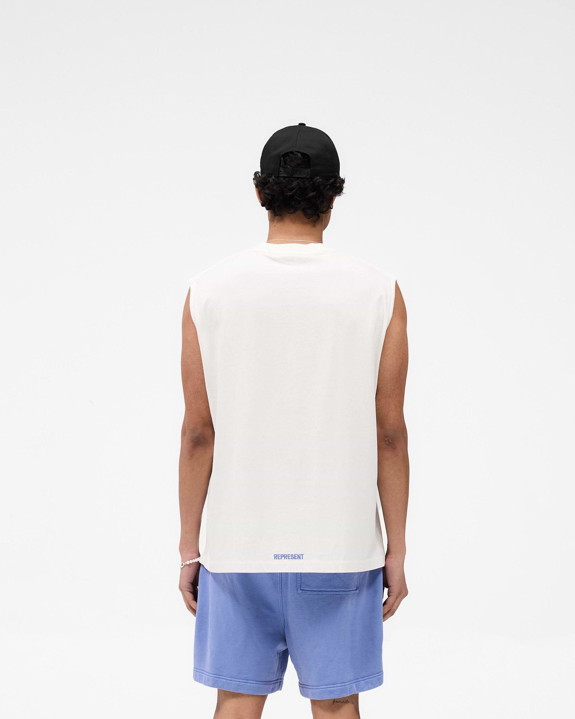 Man wearing an oversized white tank top on a plain white background | Competition Department Tank in Flat White | Oversized tank top with chest graphic and raw-edge hem | SS25 T-Shirts | Represent Clo