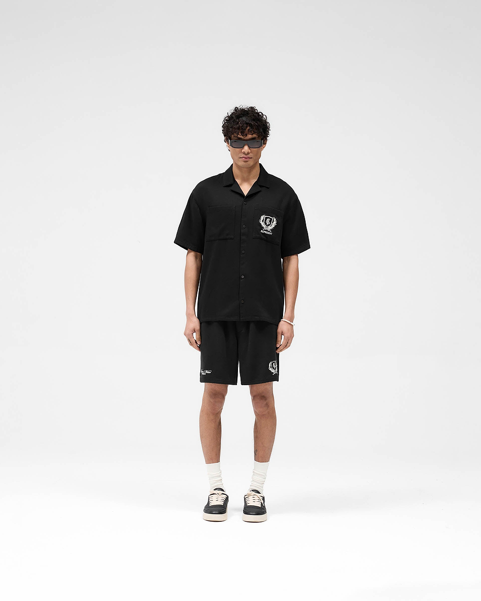 Man wearing a black short-sleeve shirt on a plain white background | Represent Crest Shirt in Jet Black | Shirt with chest pockets and embroidered graphics | SS25 Shirts | Represent Clo