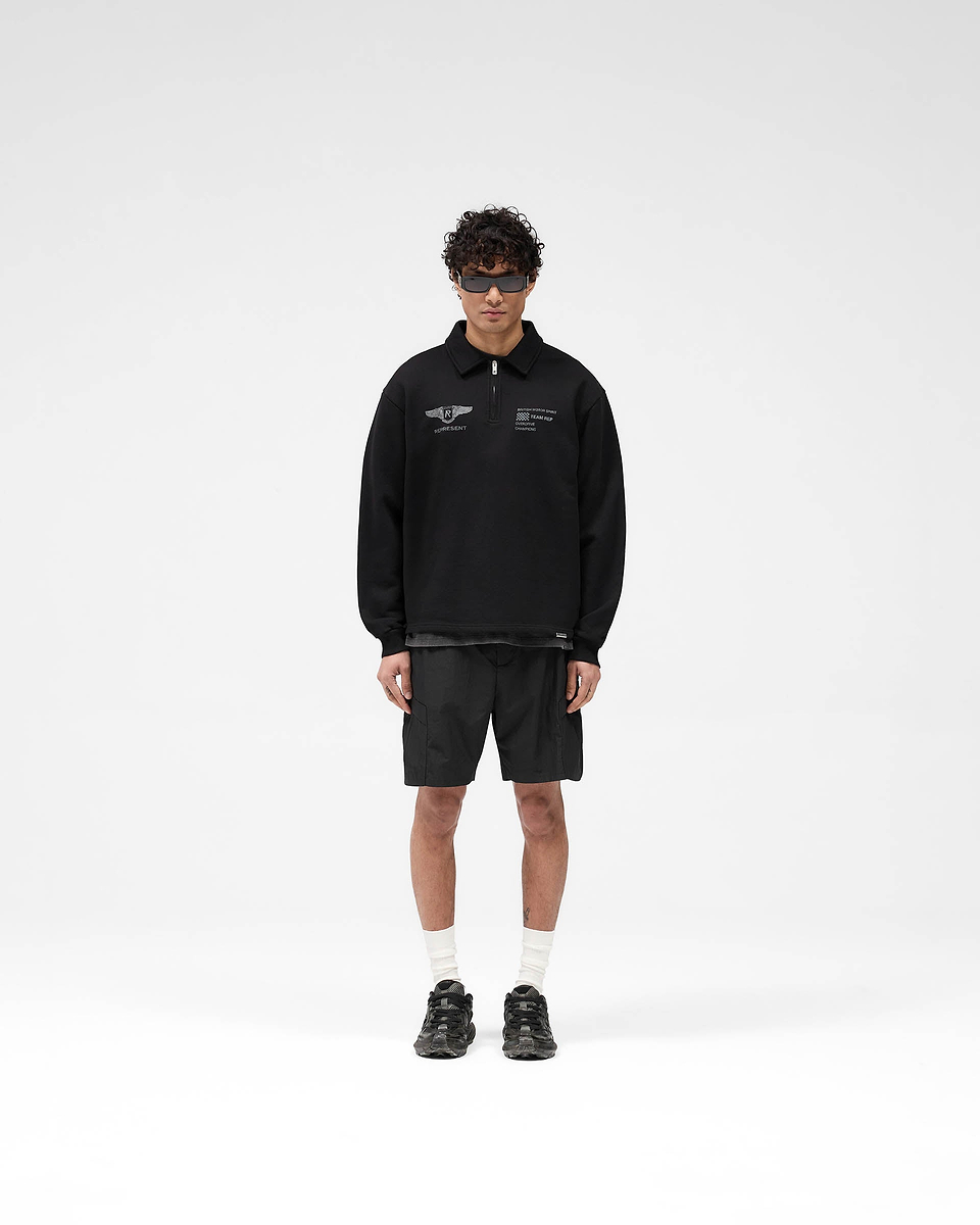 Man wearing an oversized black sweater with vintage graphics on a plain white background | Team Rep Quarter Zip in Jet Black | Quarter zip sweater with Represent branded zip | SS25 Sweaters | Represent Clo