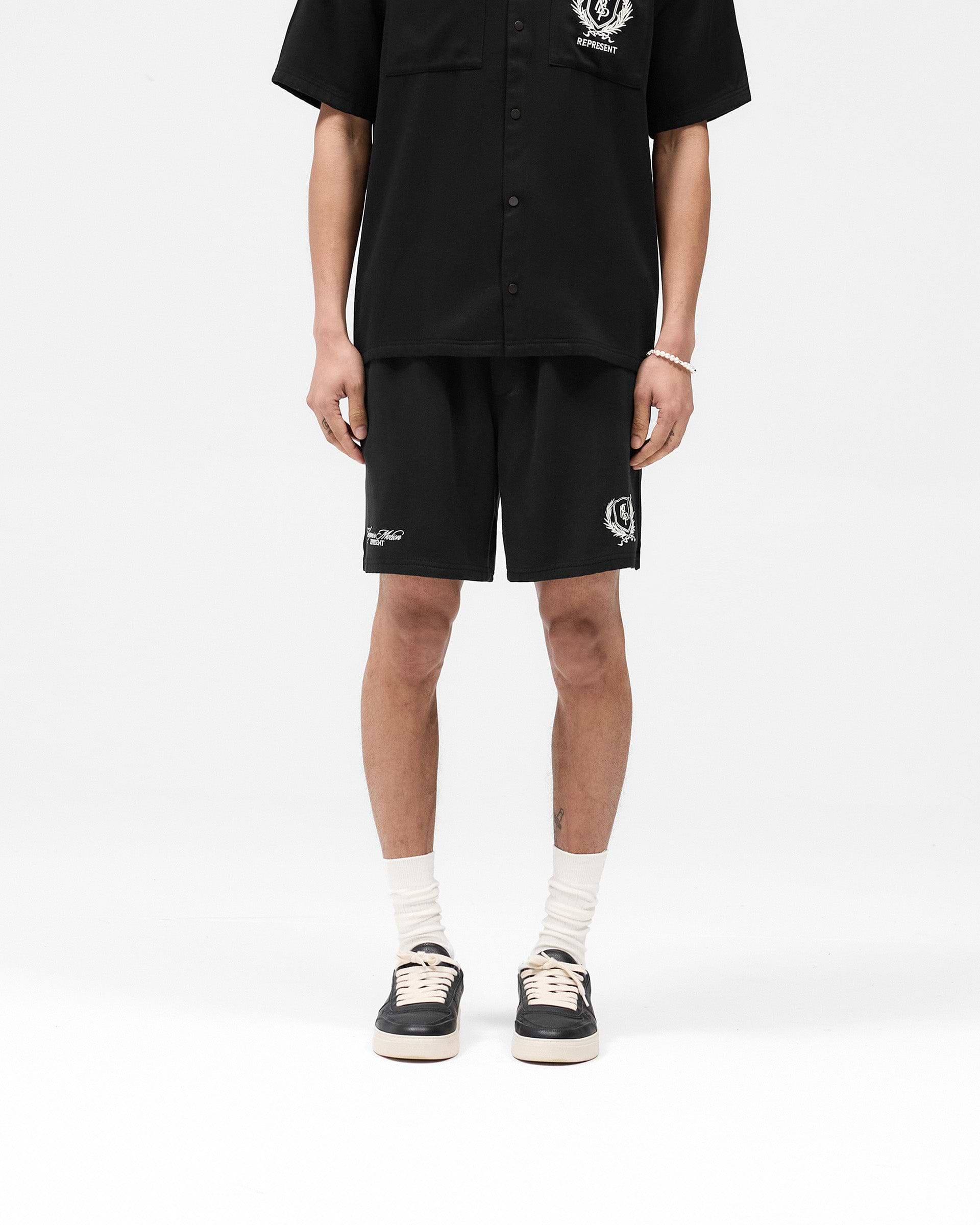 Man wearing black shorts on a plain white background | Represent Crest Short in Jet Black | Shorts with crest embroidery and elasticated waistband | SS25 Shorts | Represent Clo
