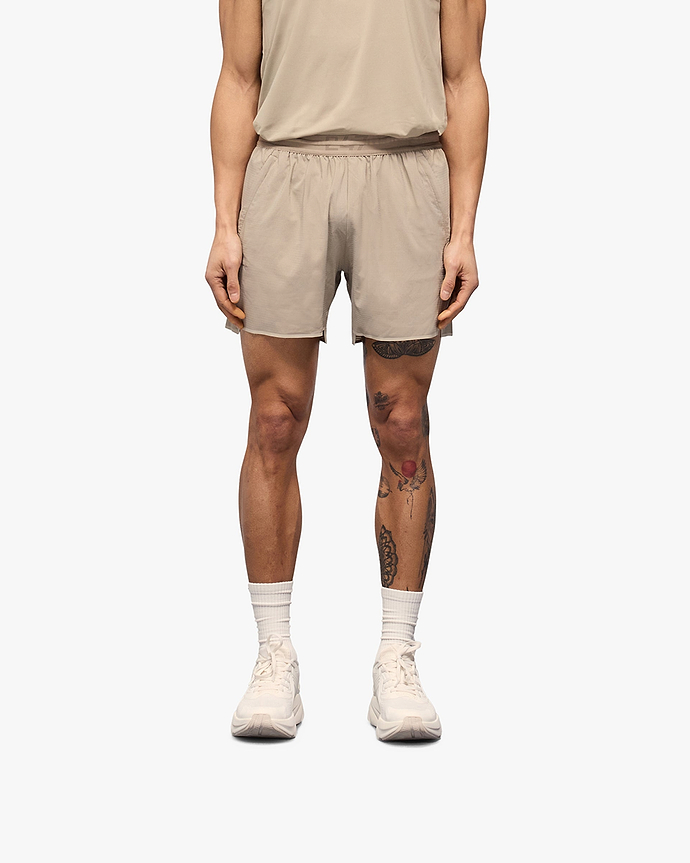 Man wearing grey shorts on a plain white background | Team 247 Aero Shorts in Pebble | Lightweight running shorts with branded waistband and zip pockets | 247 Shorts | Represent Clo