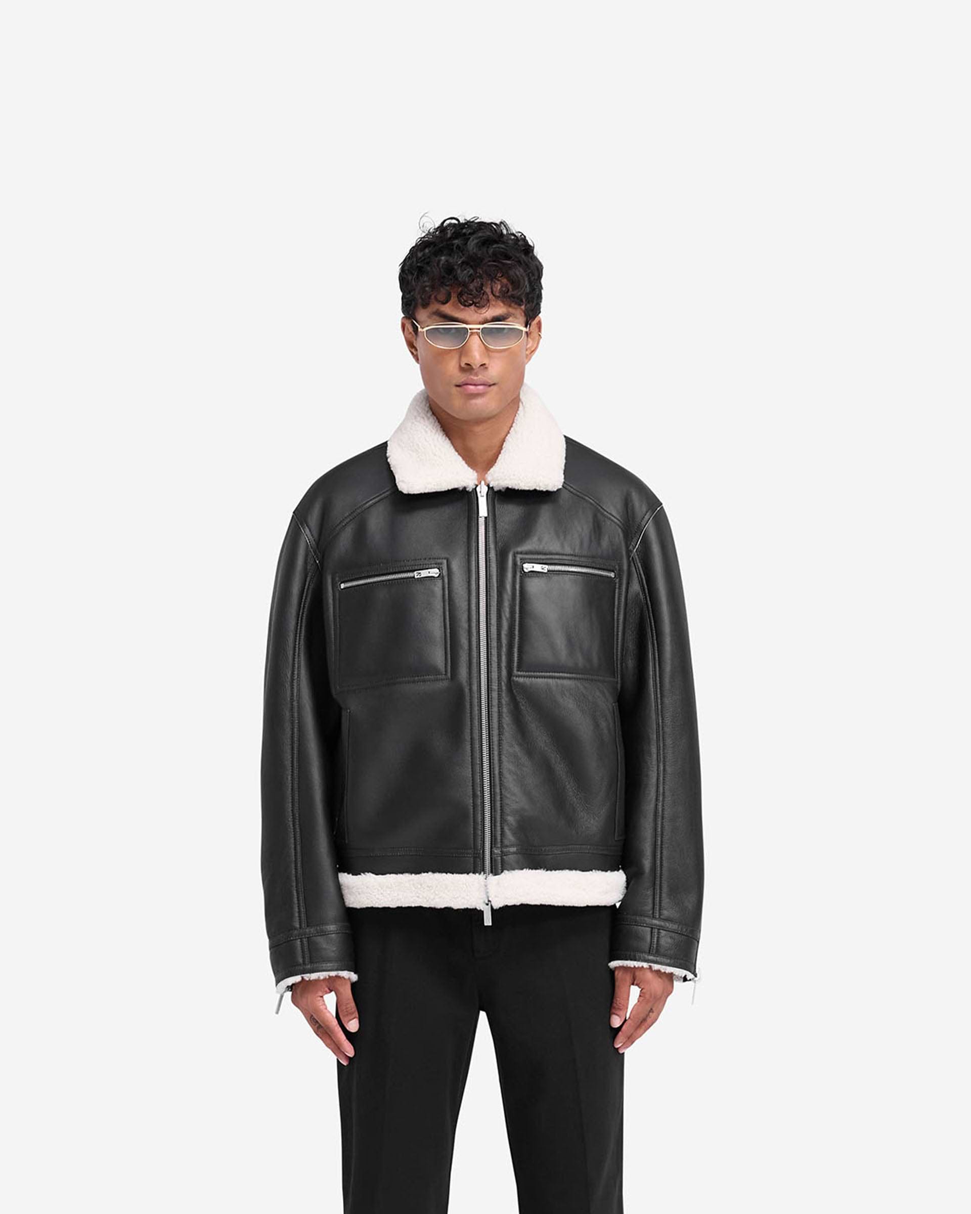 Man wearing a black shearling jacket on a plain white background | Reversible Shearling Jacket in Black | Luxury shearling and leather jacket with reversible design | FW24 Outerwear | Represent Clo