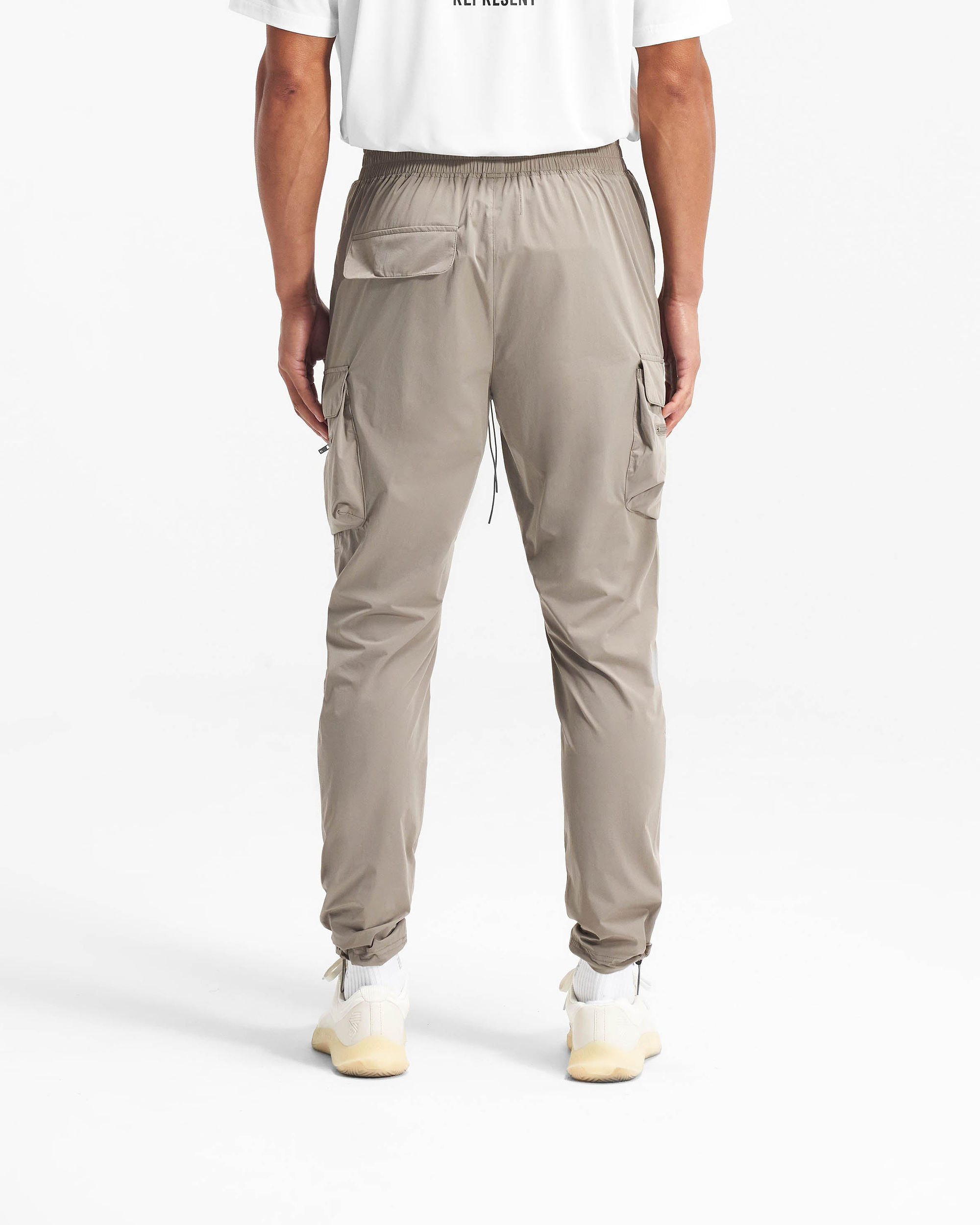 Man wearing taupe cargo pants on a plain white background | 247 Pant in Taupe | Cargo pants with elasticated waistband and zip side pockets | 247 Pants | Represent Clo