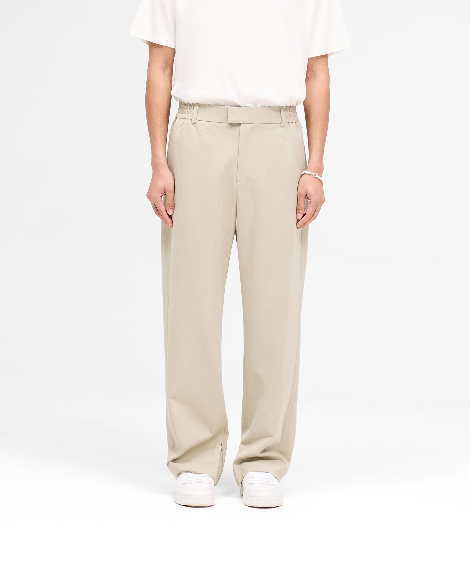 Man wearing oatmeal tailored trousers on a plain white background | Smoking Pant in Oatmeal | Slim fit pants with pressed front creases | SS25 Pants | Represent Clo