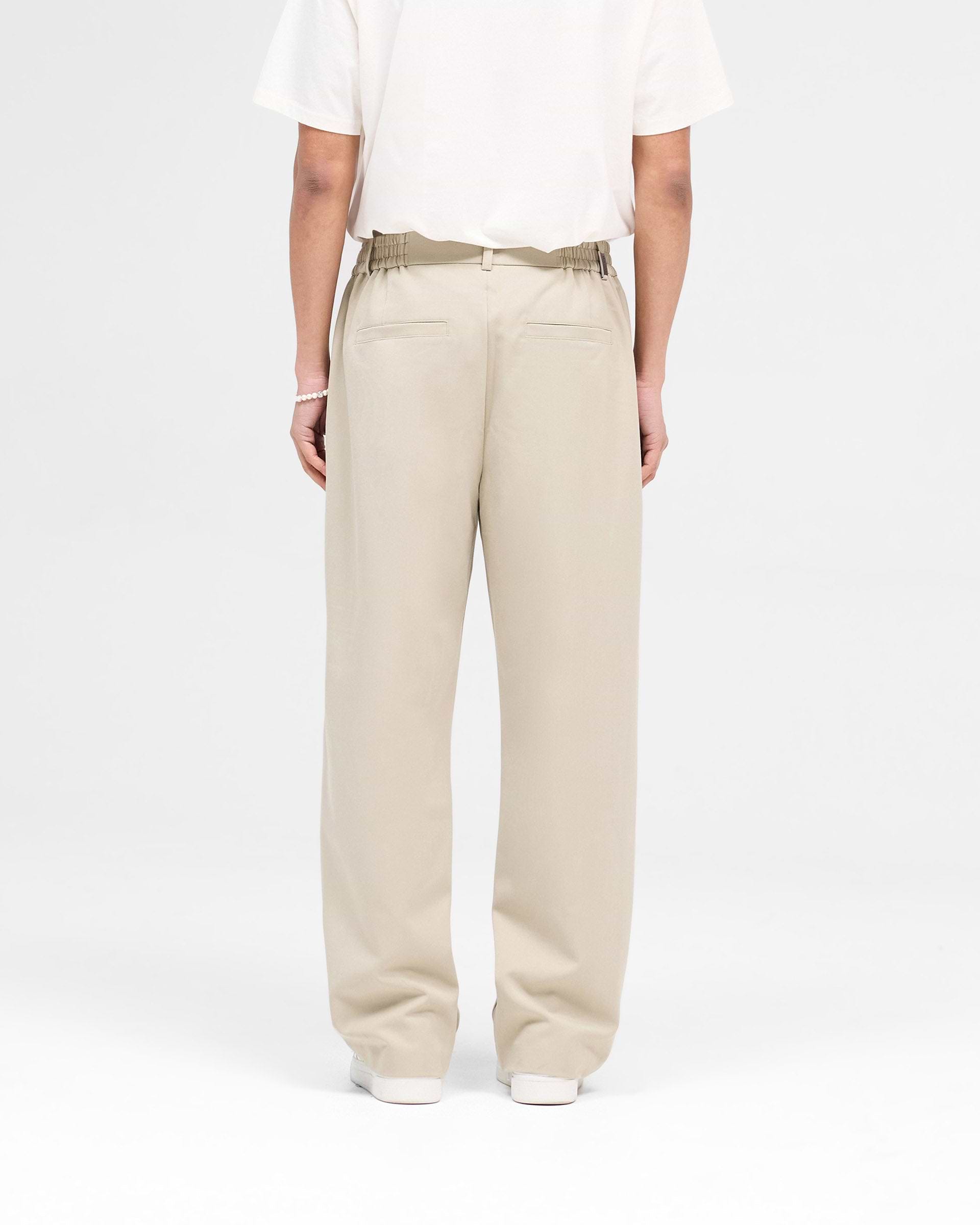 Man wearing oatmeal coloured trousers on a plain white background | Smoking Pant in Oatmeal | Slightly cropped slim fit trousers with pressed creases | SS25 Pants | Represent Clo