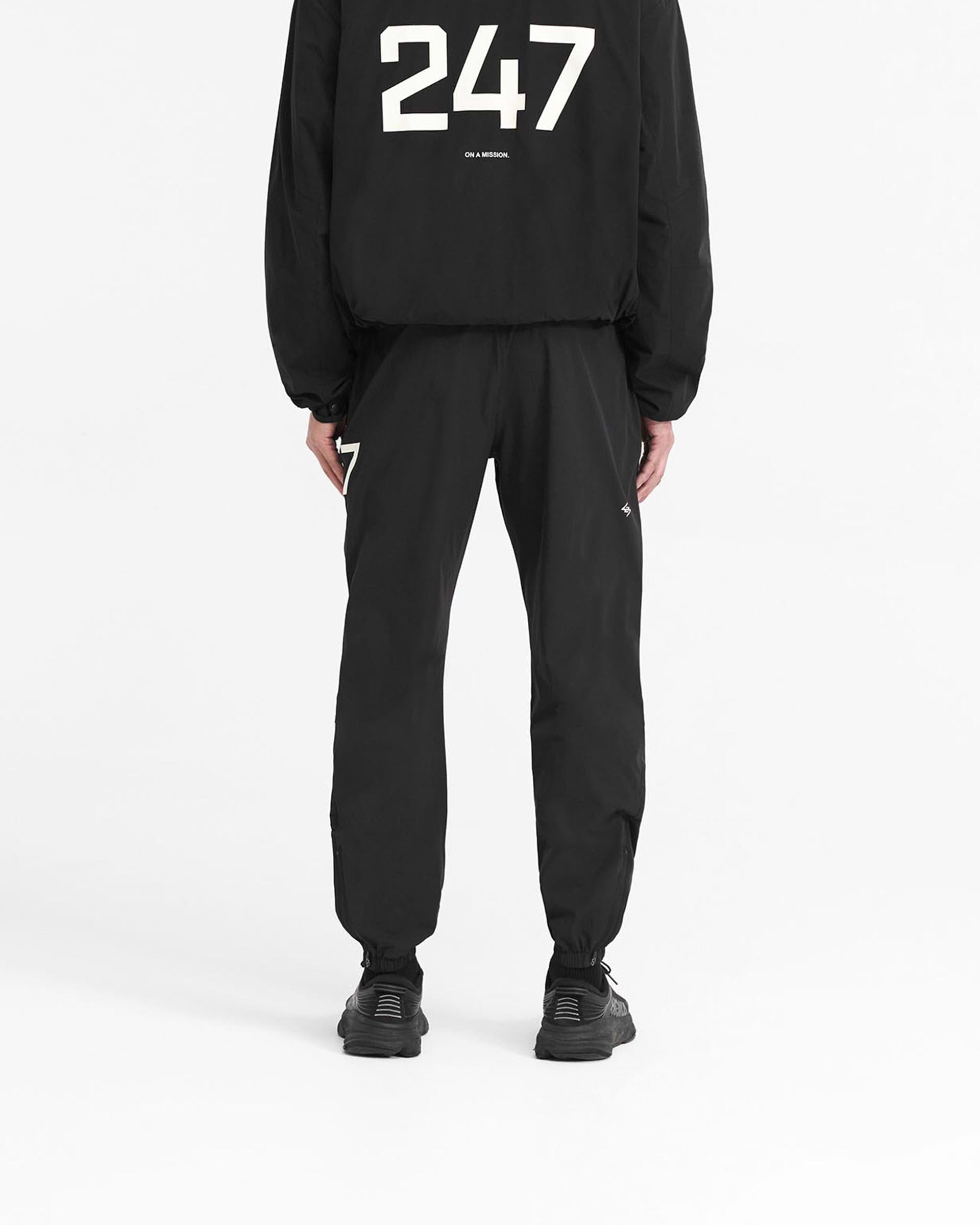 Man wearing black training pants on a plain white background | 247 Training Pant in Jet Black | Athletic pants with elasticated waistband and zip cuffs | 247 Pants | Represent Clo