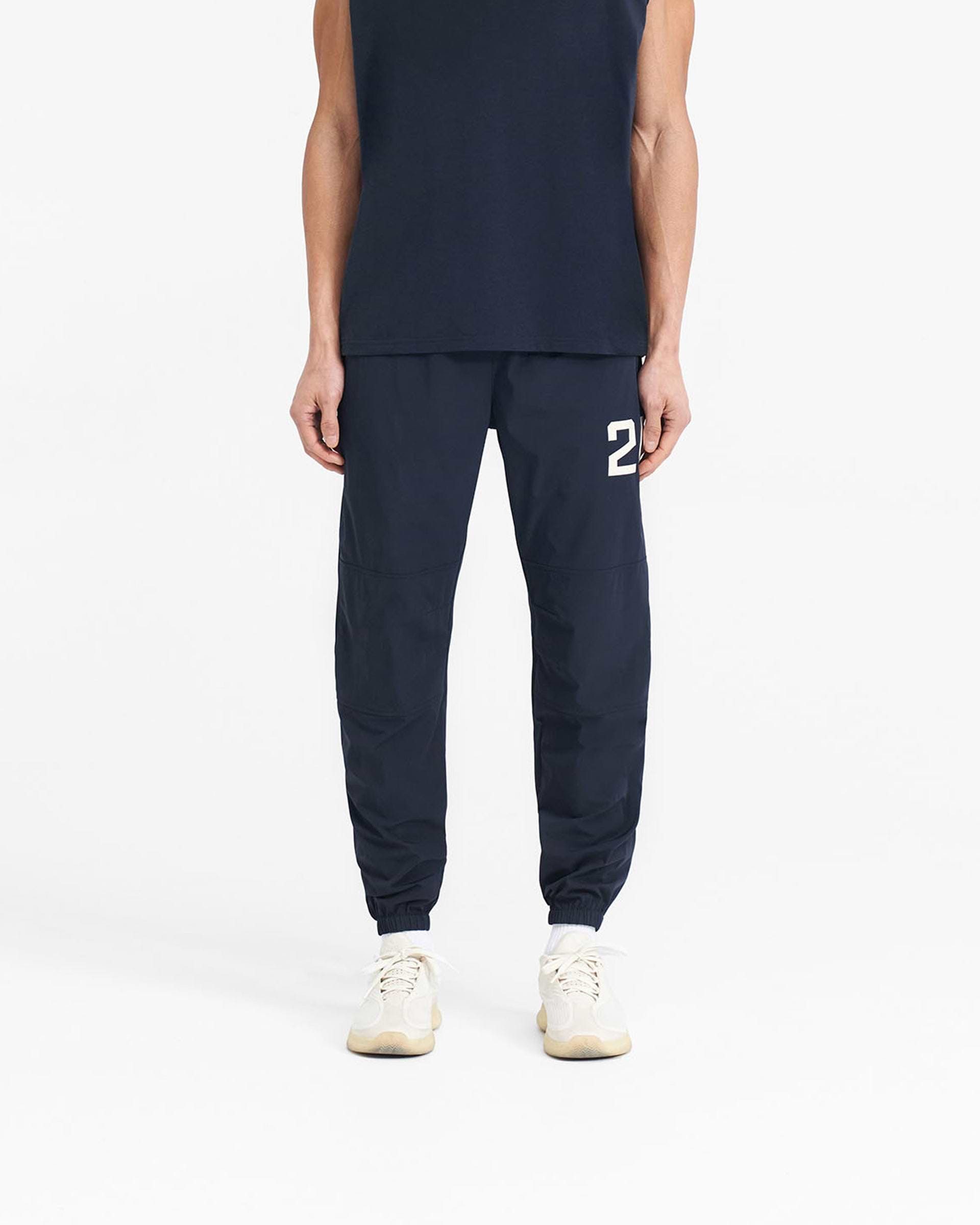 Man wearing navy pants on a plain white background | 247 Training Pant in Navy | Training pants with elasticated waistband and zip pockets | 247 Pants | Represent Clo