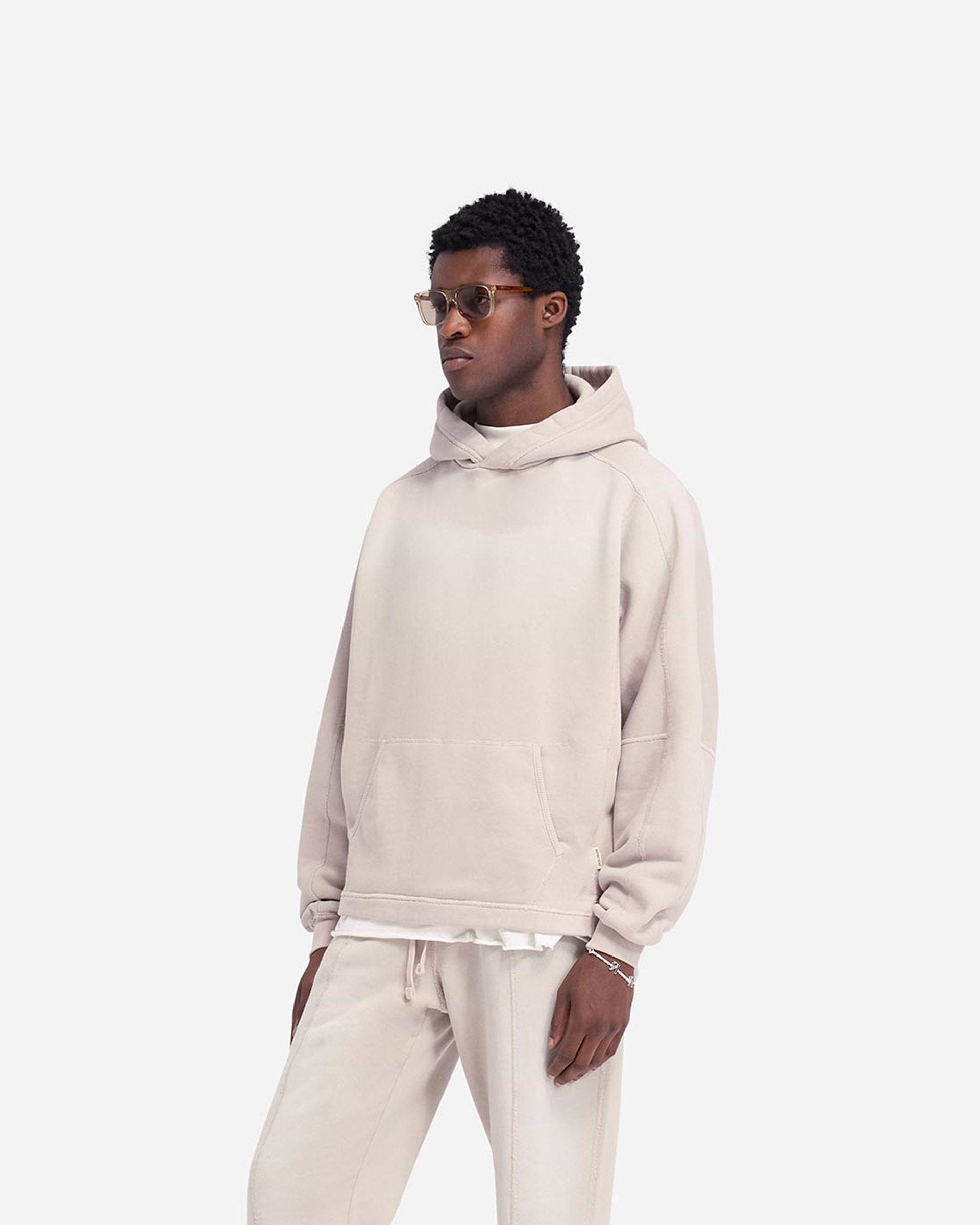 Man wearing an oversized oat hoodie on a plain white background | Stepped Hem Hoodie in Oat | Oversized hoodie with sun fade wash and stepped hem | FW24 Hoodies | Represent Clo