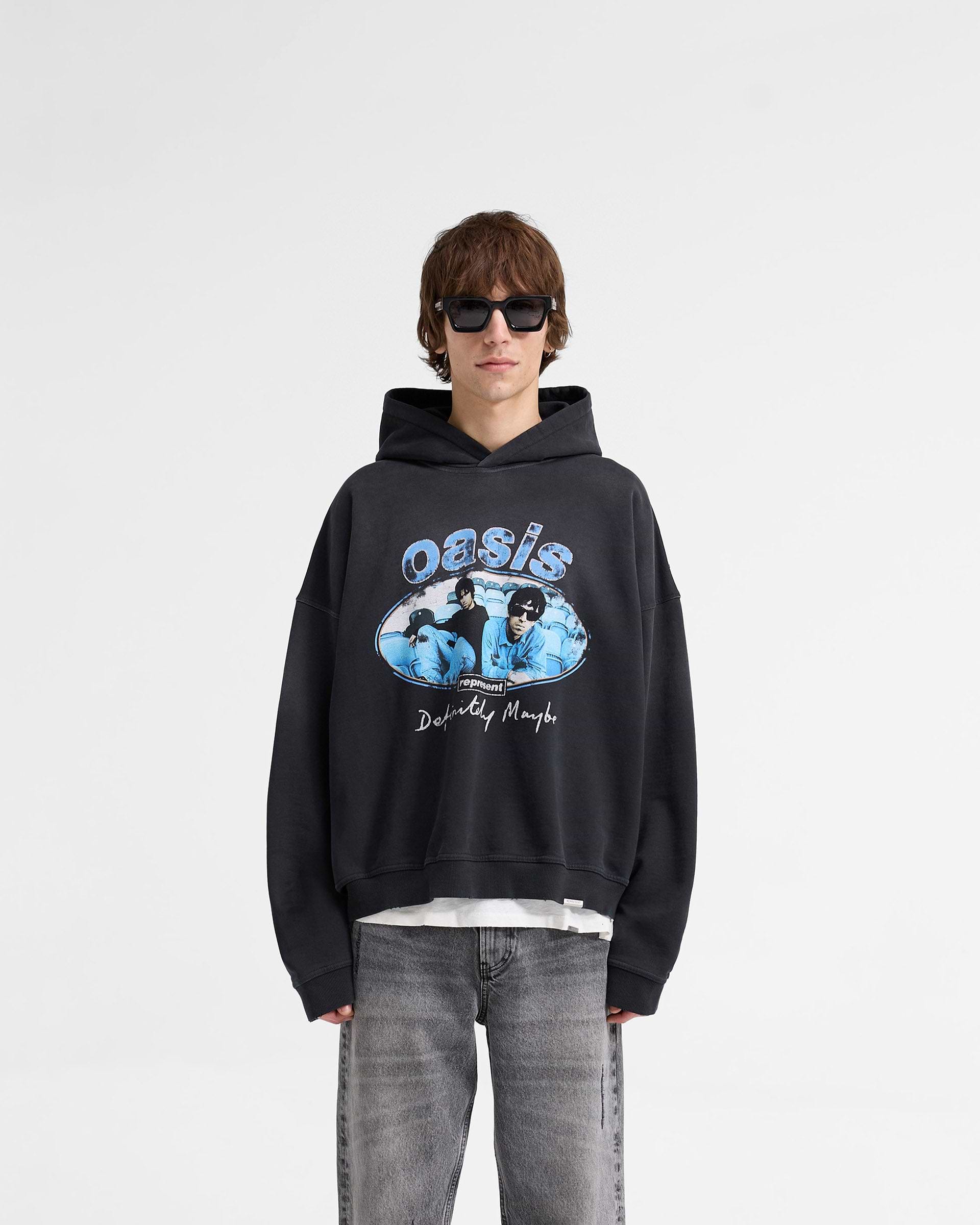 Man wearing a black hoodie with vintage distressed details on a plain white background | Represent X Oasis Maine Road Hoodie in Washed Black | Oversized hoodie with iconic Oasis imagery and concert ticket detail | FW24 Hoodies | Represent Clo
