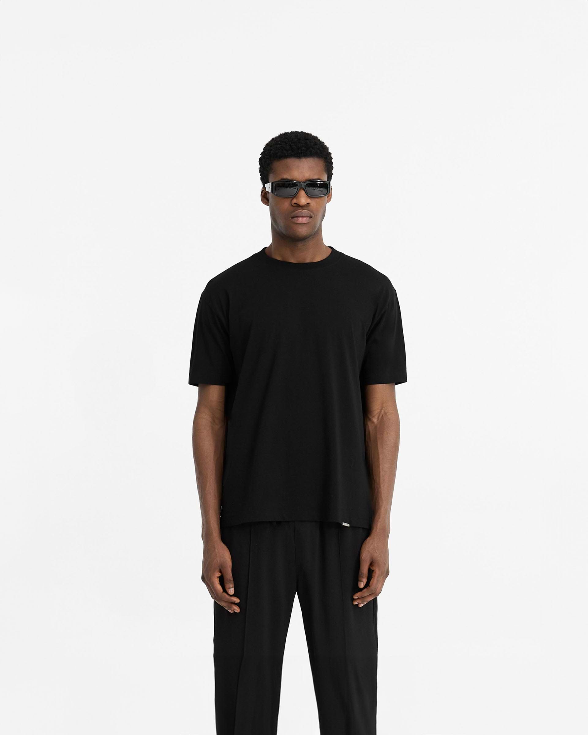 Man wearing a black t-shirt on a plain white background | Initial T-Shirt in Black | Slim fit t-shirt with embroidered Initial and metal bar logo | Initial T-Shirts | Represent Clo