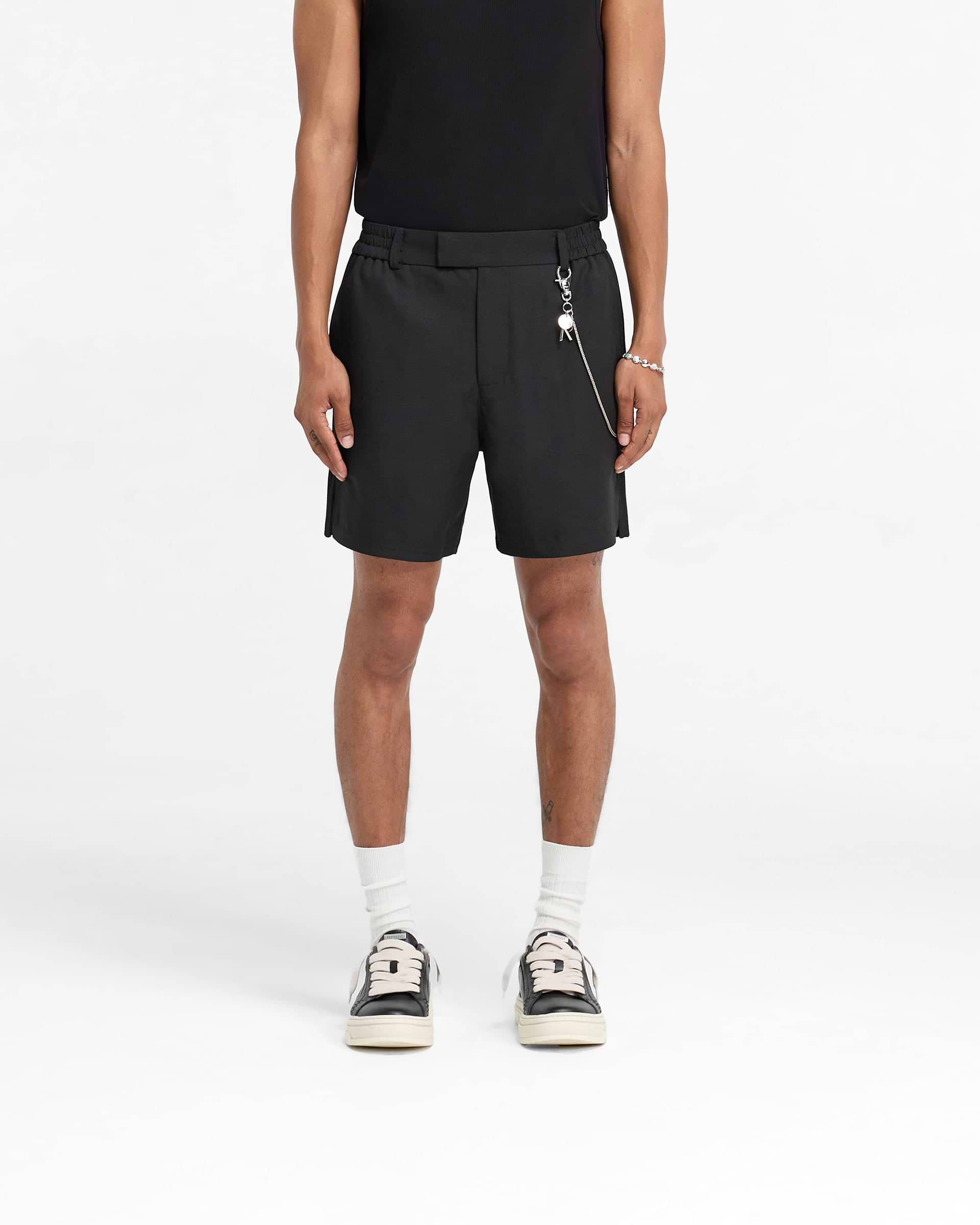 Man wearing black shorts on a plain white background | Logo Yacht Short in Black | Linen blend shorts with hybrid waistband and side split hem | FW24 Shorts | Represent Clo