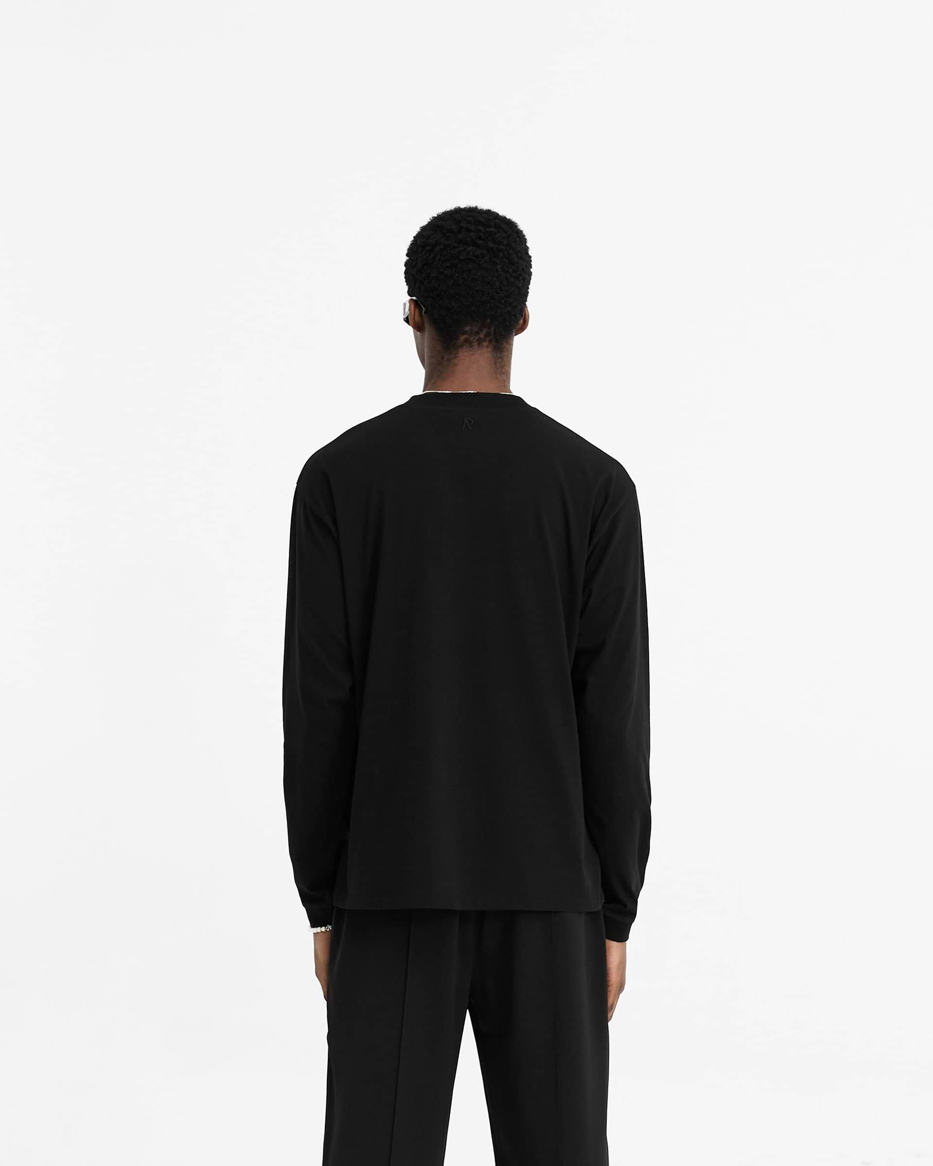 Man wearing a black long sleeve t-shirt on a plain white background | Initial Long Sleeve T-Shirt in Black | Regular fit long sleeve t-shirt with embroidered details | Initial T-Shirts | Represent Clo