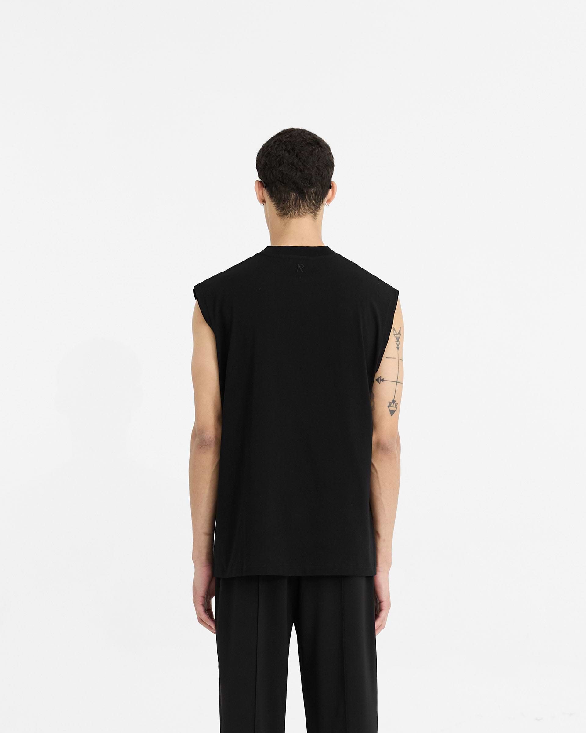 Man wearing a black boxy tank on a plain white background | Initial Boxy Tank in Black | Oversized and boxy cropped tank | Initial T-Shirts | Represent Clo