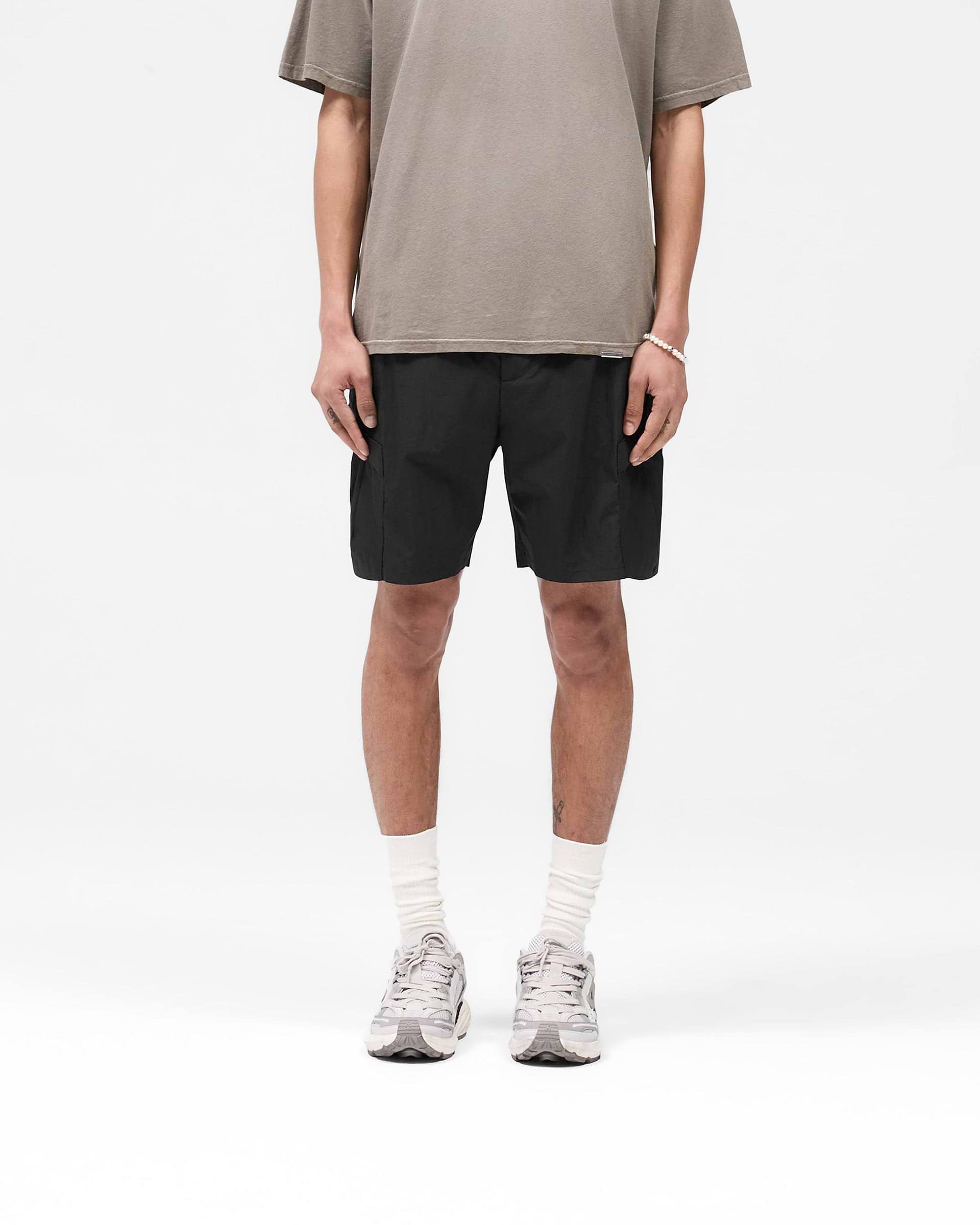 Man wearing black cargo shorts on a plain white background | Tech Cargo Short in Jet Black | Lightweight shorts with pleated cargo pockets | SS25 Shorts | Represent Clo