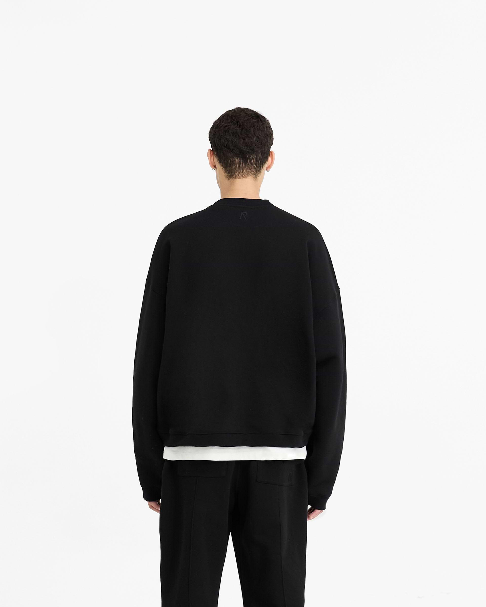 Man wearing a black boxy sweater on a plain white background | Initial Boxy Sweater in Black | Oversized sweater with cropped body and dropped shoulders | Initial Sweaters | Represent Clo