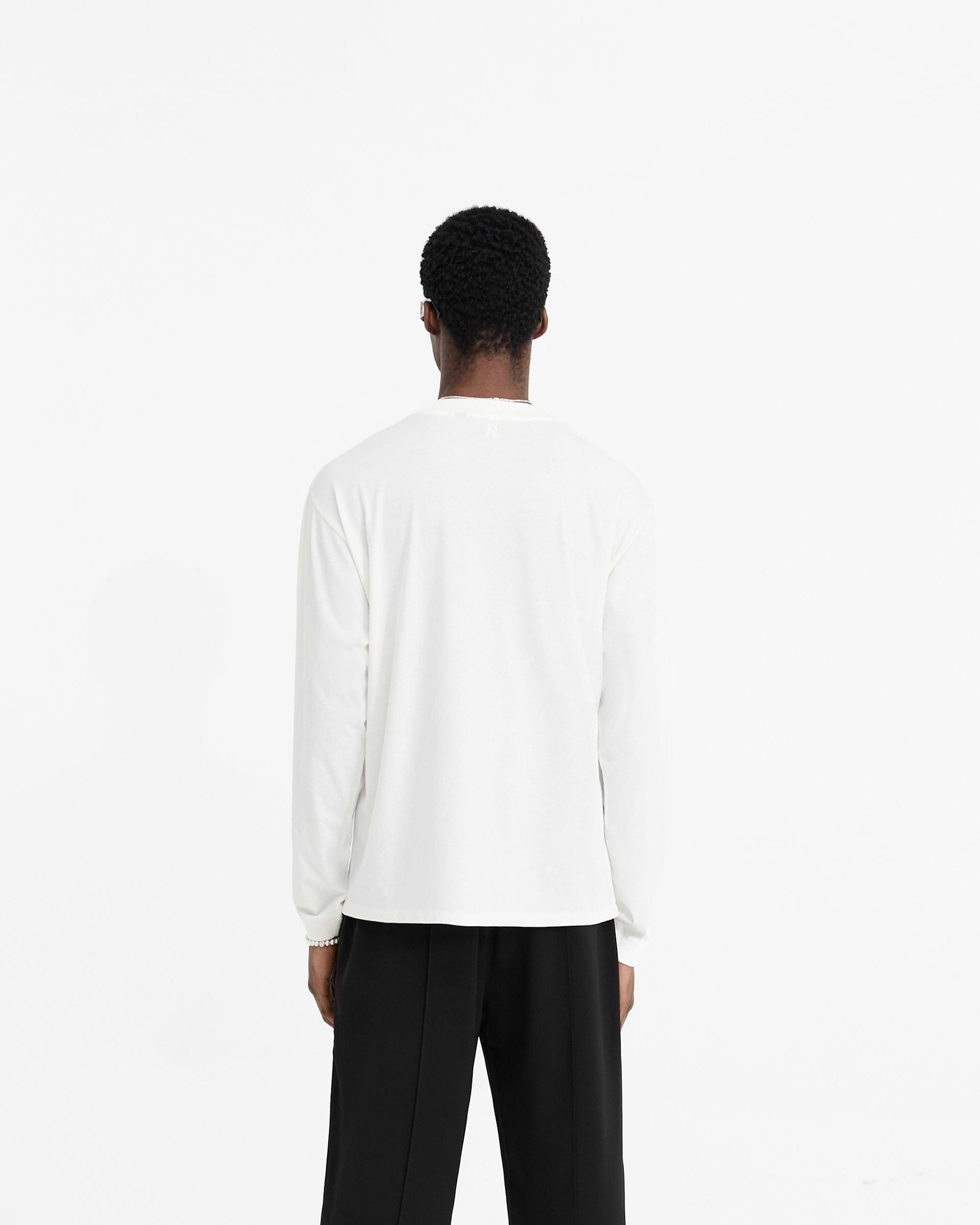 Man wearing a white long sleeve t-shirt on a plain white background | Initial Long Sleeve T-Shirt in Flat White | Regular fit cotton t-shirt with ribbed cuffs and collar | Initial T-Shirts | Represent Clo