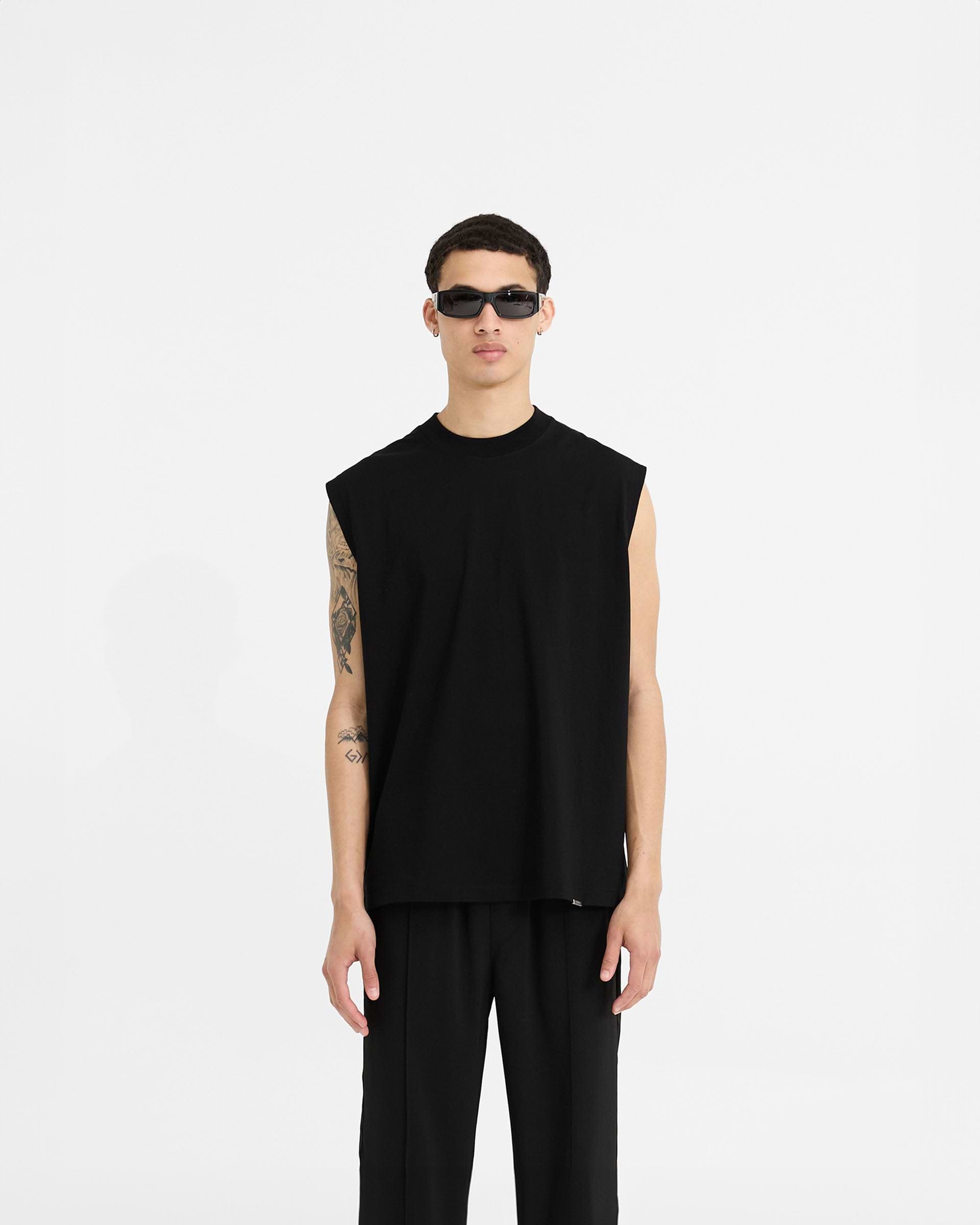 Man wearing a black boxy tank top on a plain white background | Initial Boxy Tank in Black | Oversized cropped tank with ribbed collar | Initial T-Shirts | Represent Clo