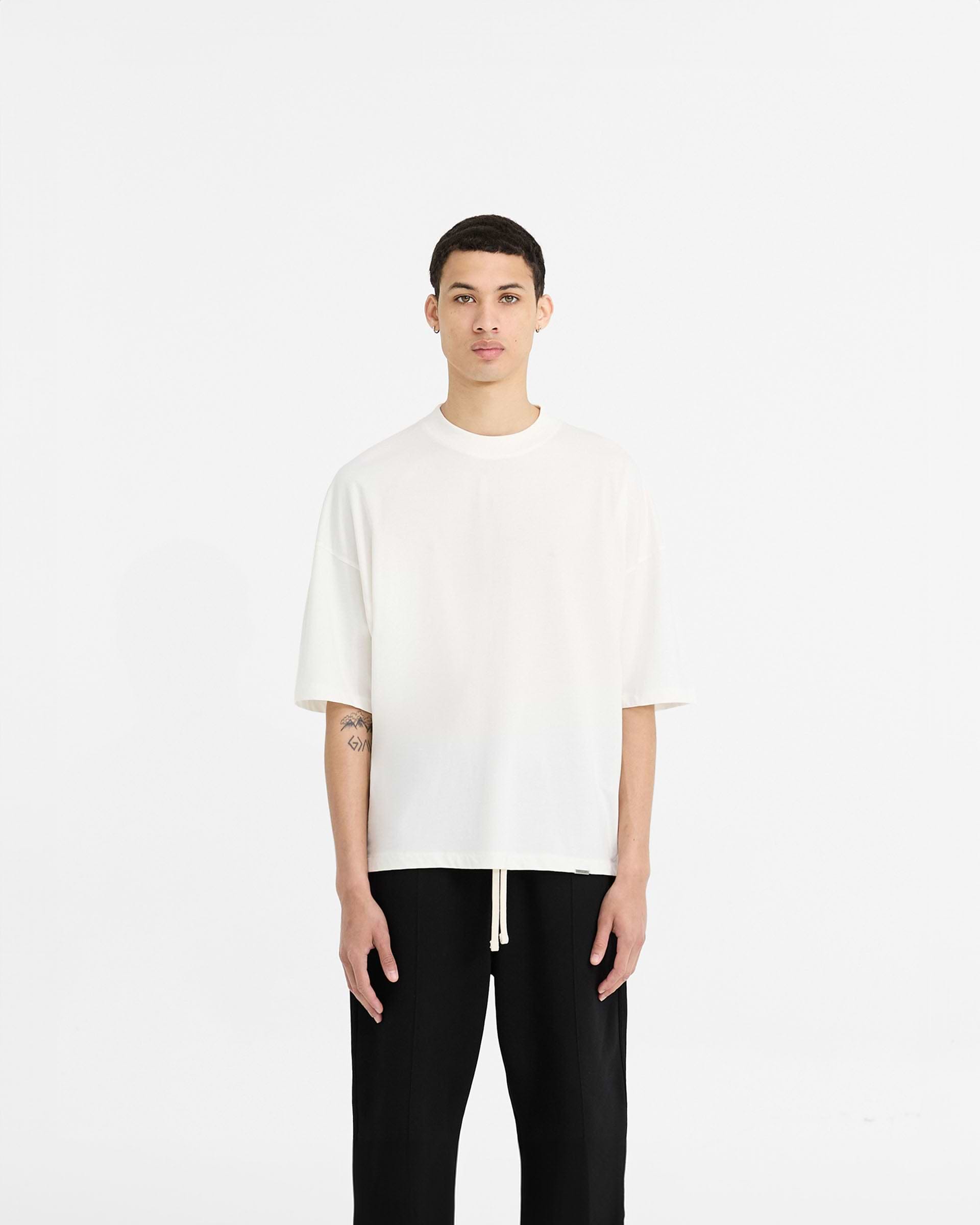 Man wearing a white t-shirt on a plain white background | Initial Boxy T-Shirt in Flat White | Oversized and boxy cropped t-shirt | Initial T-Shirts | Represent Clo