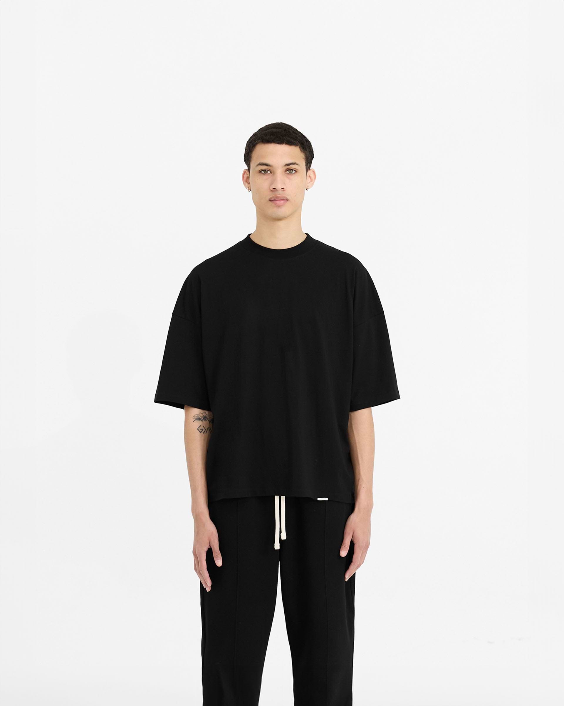Man wearing a black oversized t-shirt on a plain white background | Initial Boxy T-Shirt in Black | Boxy cropped t-shirt with embroidered details | Initial T-Shirts | Represent Clo