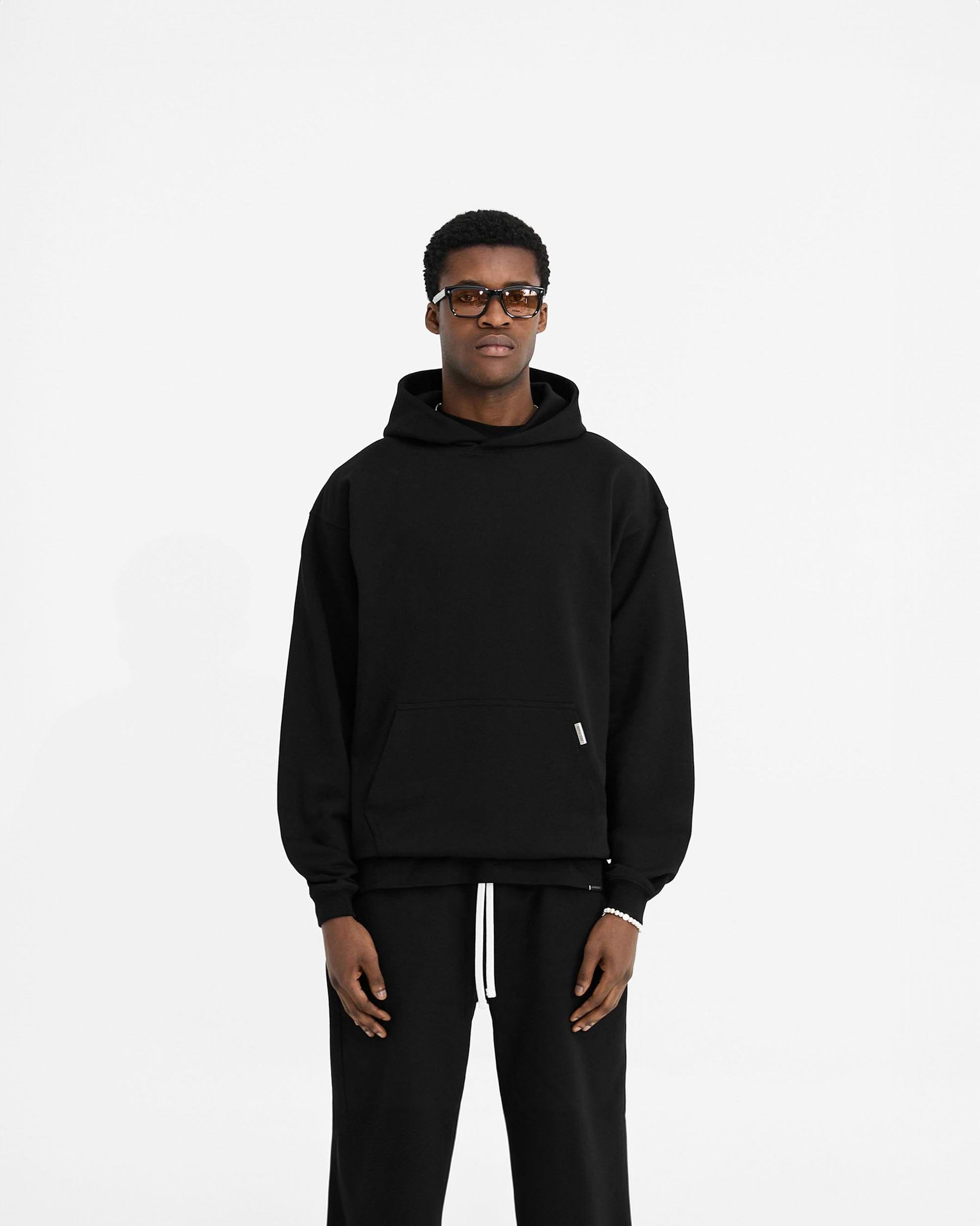 Man wearing a black oversized hoodie on a plain white background | Initial Oversized Hoodie in Black | Heavyweight loopback jersey cotton hoodie | Initial Hoodies | Represent Clo