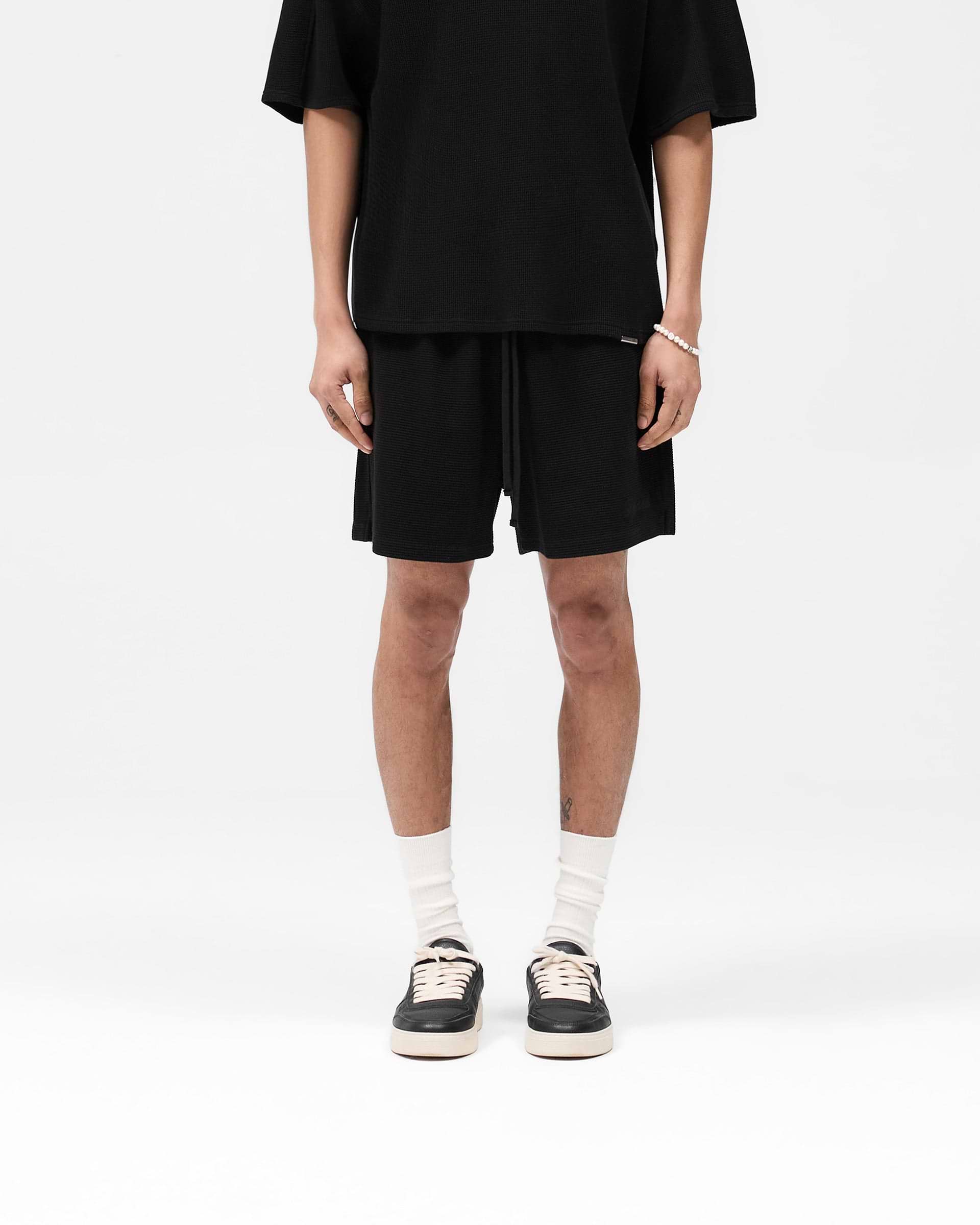Man wearing black waffle shorts on a plain white background | Waffle Shorts in Black | Heavyweight waffle fabric shorts with elasticated waistband | SS25 Shorts | Represent Clo